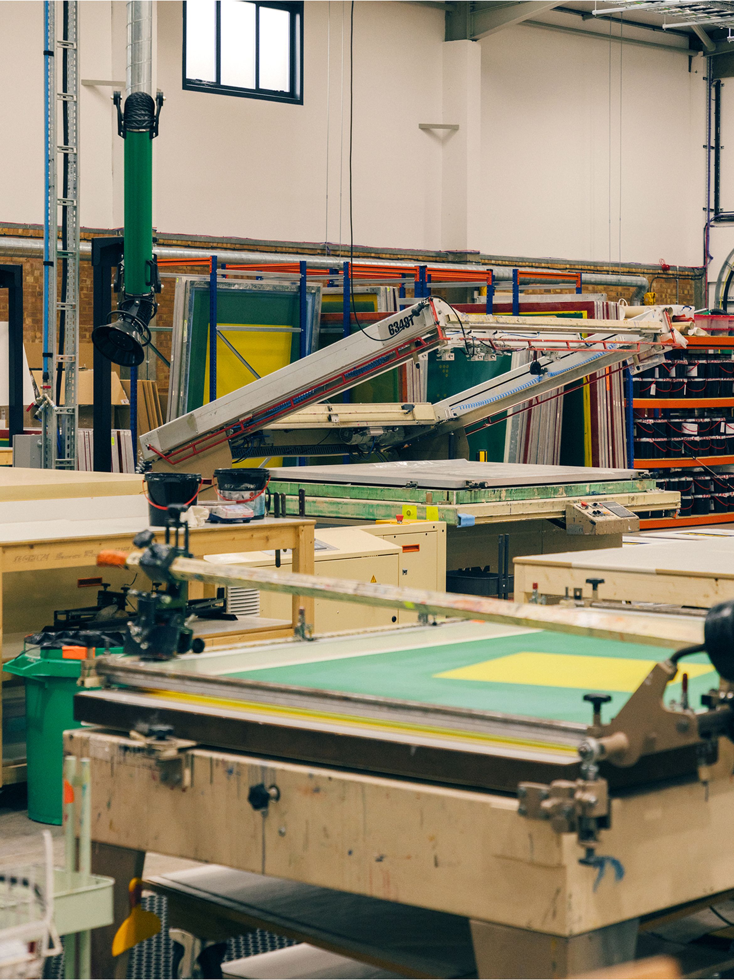 A screen printing workshop with various equipment, including screens, frames, and tables, organized in a spacious industrial setting.