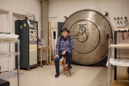 Larry Bell sat on a stool smiling in his glass work studio Larry Bell sat on a stool smiling in his glass work studio