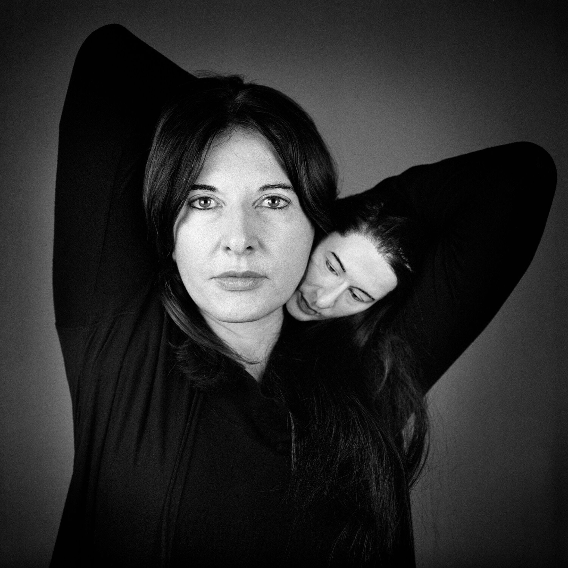 A black and white image of artist Marina Abramović, with a miniature version of her face on her shoulder.