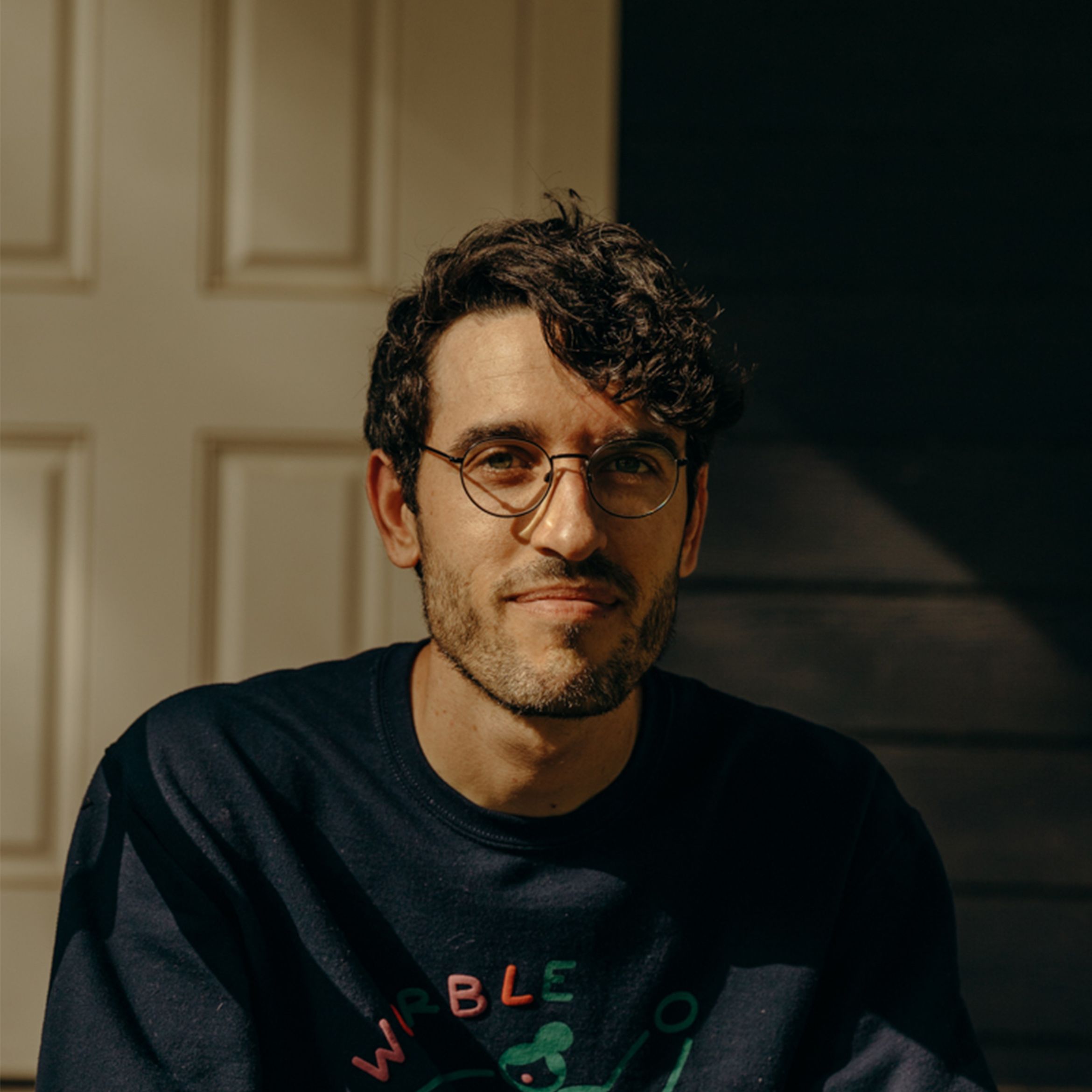 Artist Tyler Hobbs head and torso sitting partly in the sun looking at the camera