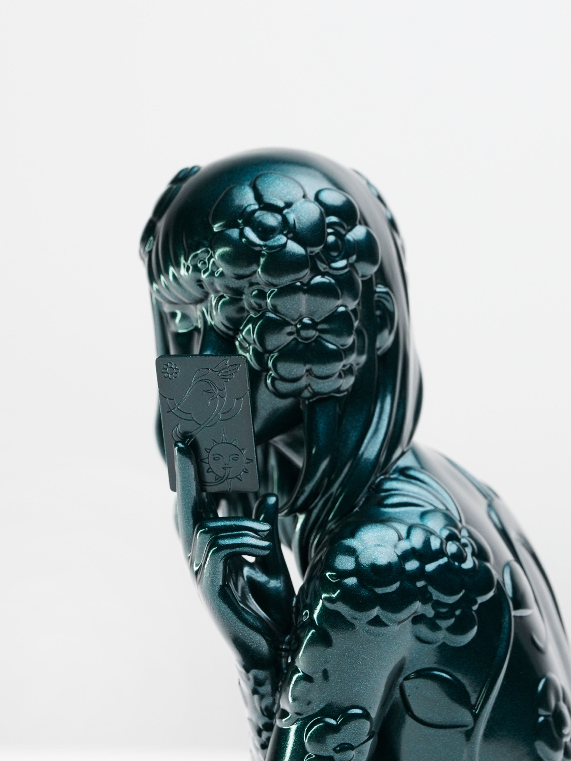 Close-up of a sculpture of a person with stylised hair and a flower detail, featuring a reflective, dark teal surface.