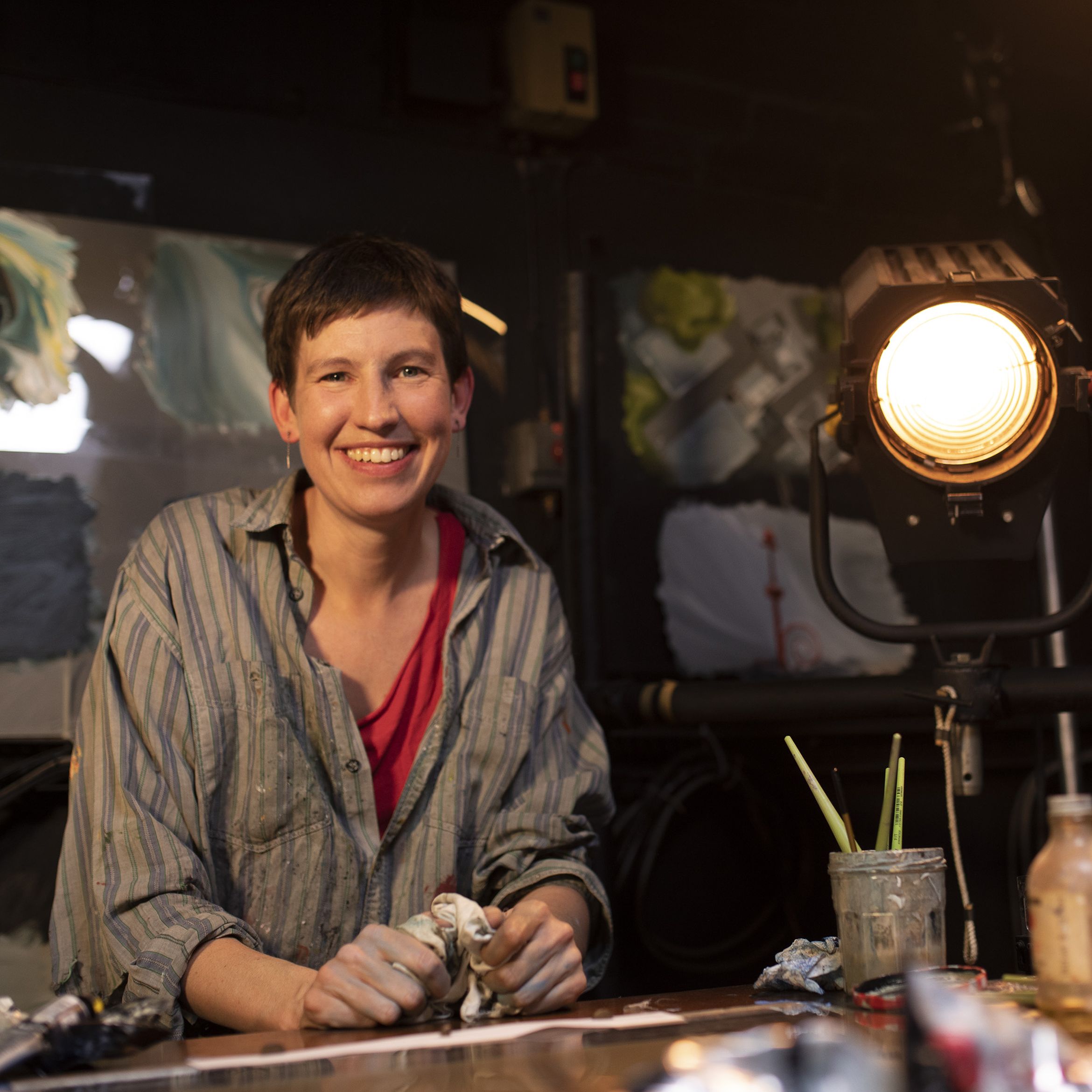 Portrait of artist Em Cooper in her studio at her desk beside a large light