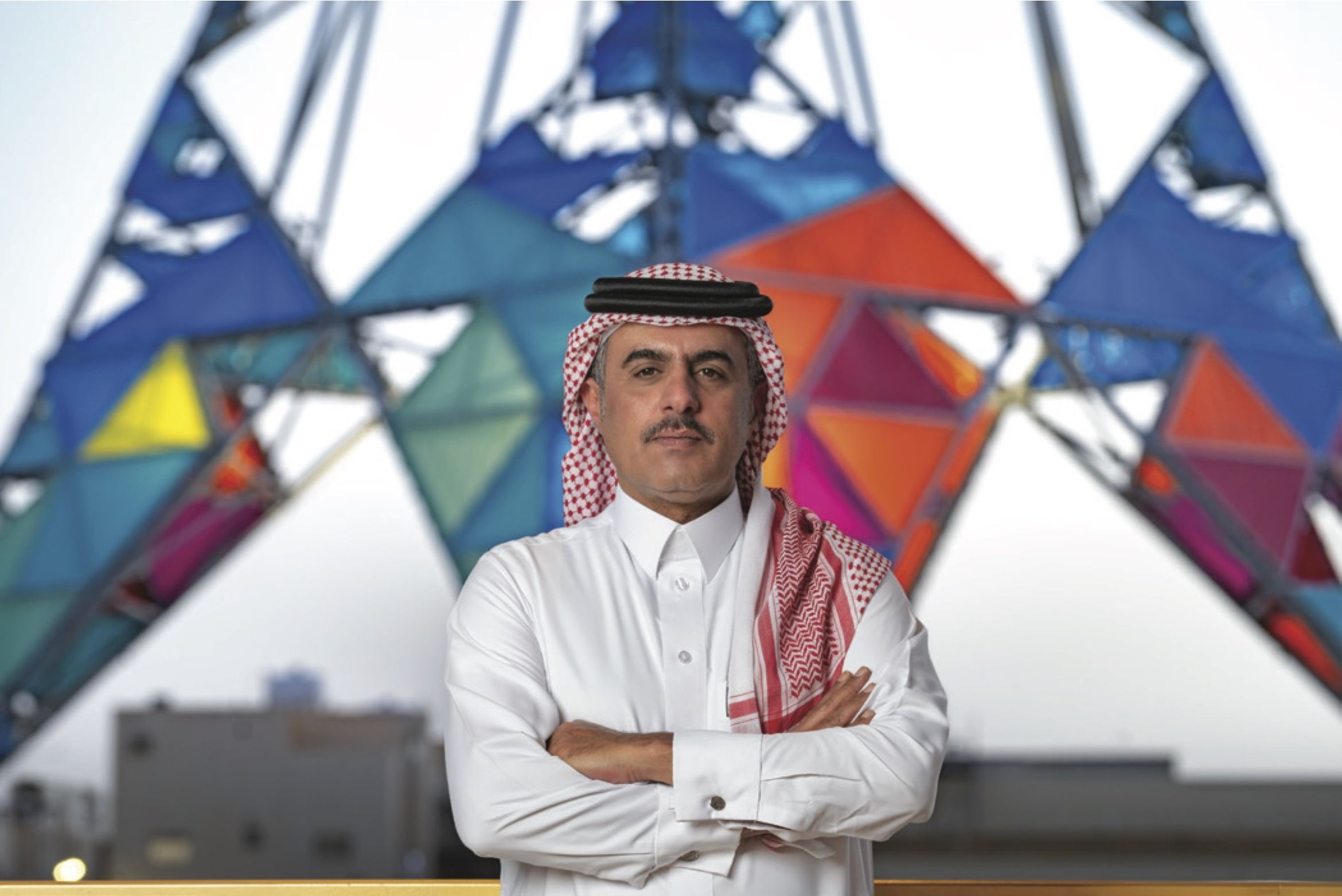Artist Abdulnasser Gharem stands with arms crossed in front of a colorful geometric structure.