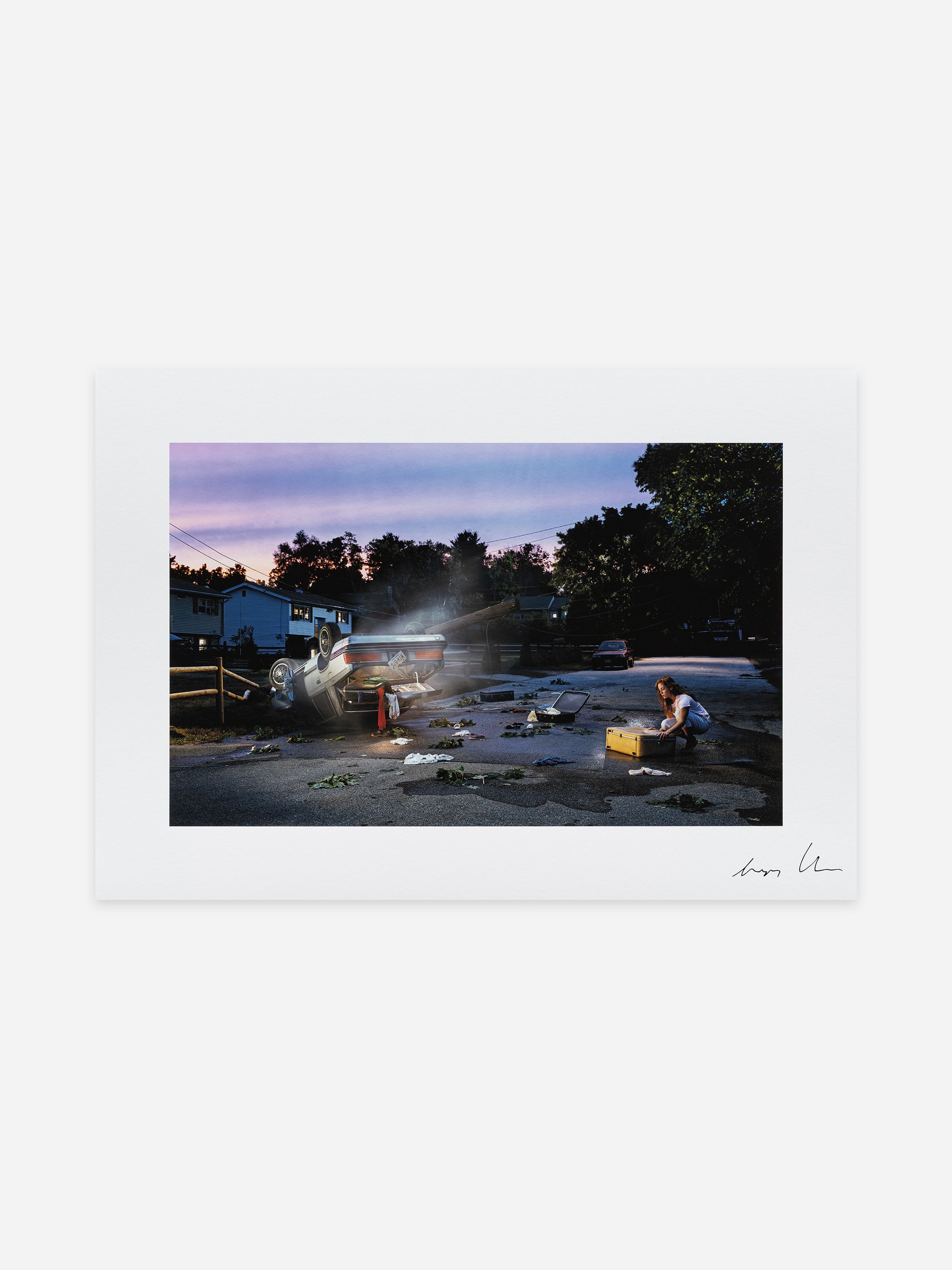 A flipped car on a suburban street at dusk, with debris scattered, and a person kneeling nearby with an open suitcase. A flipped car on a suburban street at dusk, with debris scattered, and a person kneeling nearby with an open suitcase.