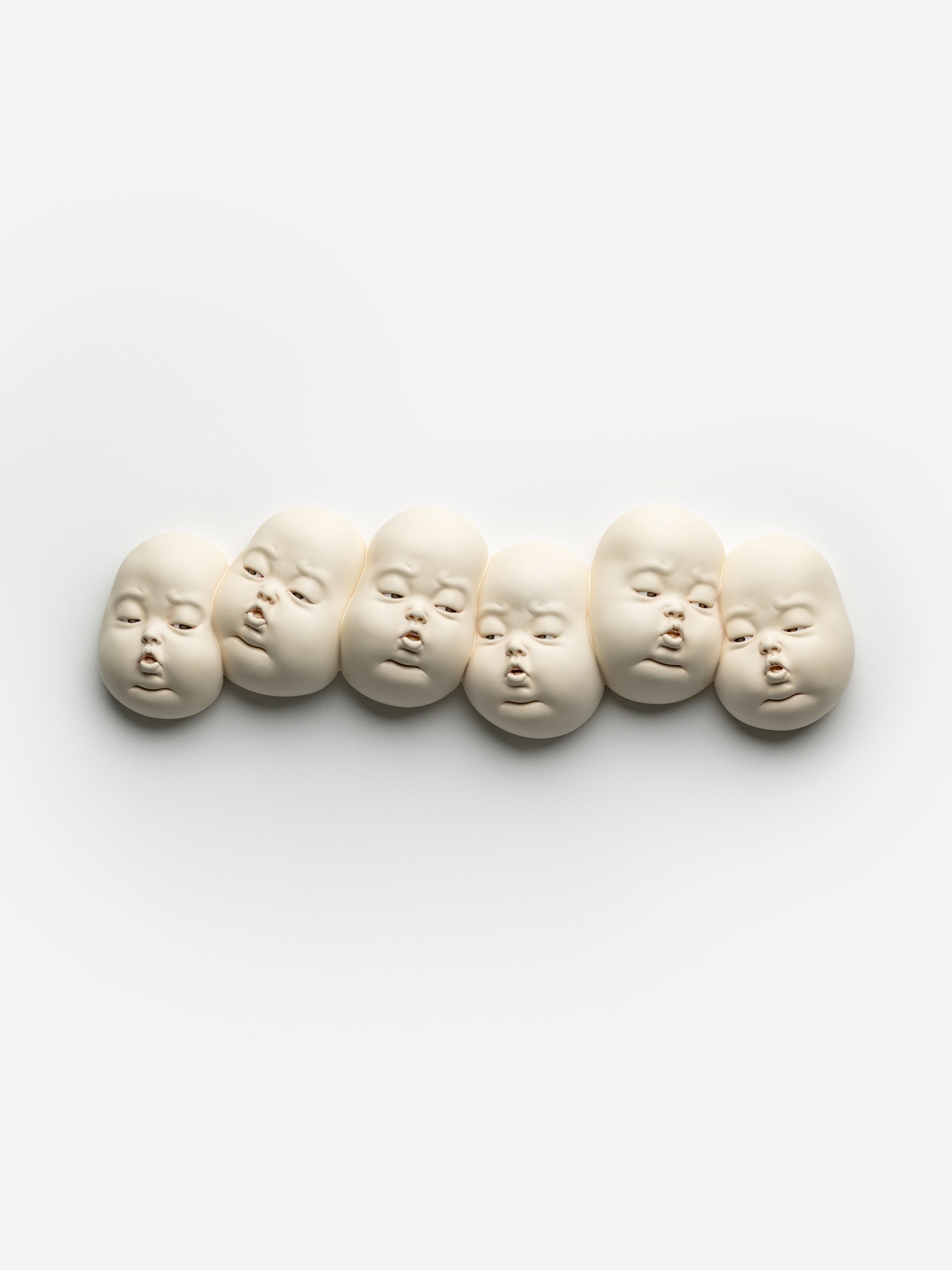 Six white doll heads with serene expressions arranged in a line on a plain background.