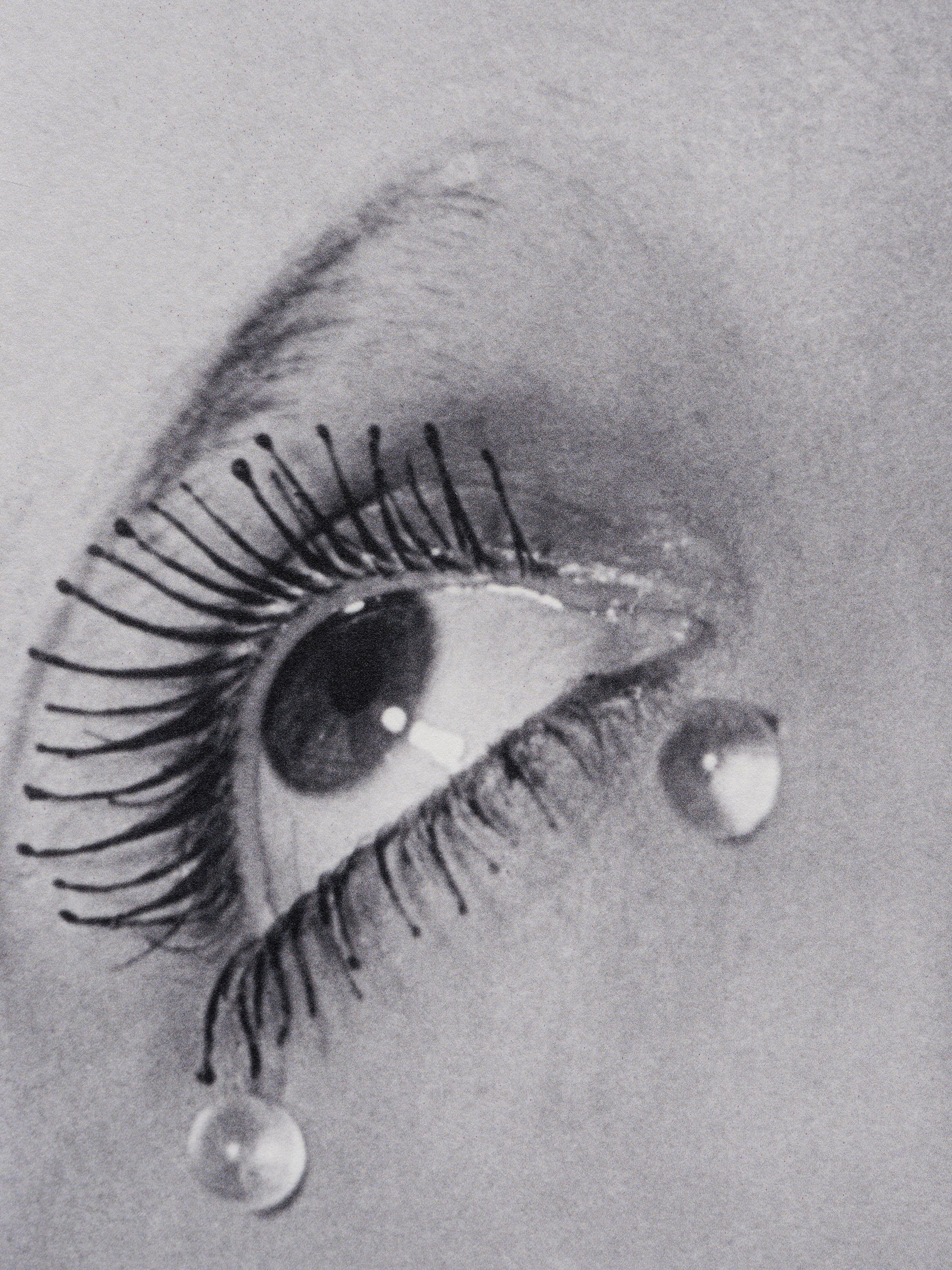 Black-and-white close-up of an eye with long, sculpted eyelashes and oversized glass-like tear droplets.