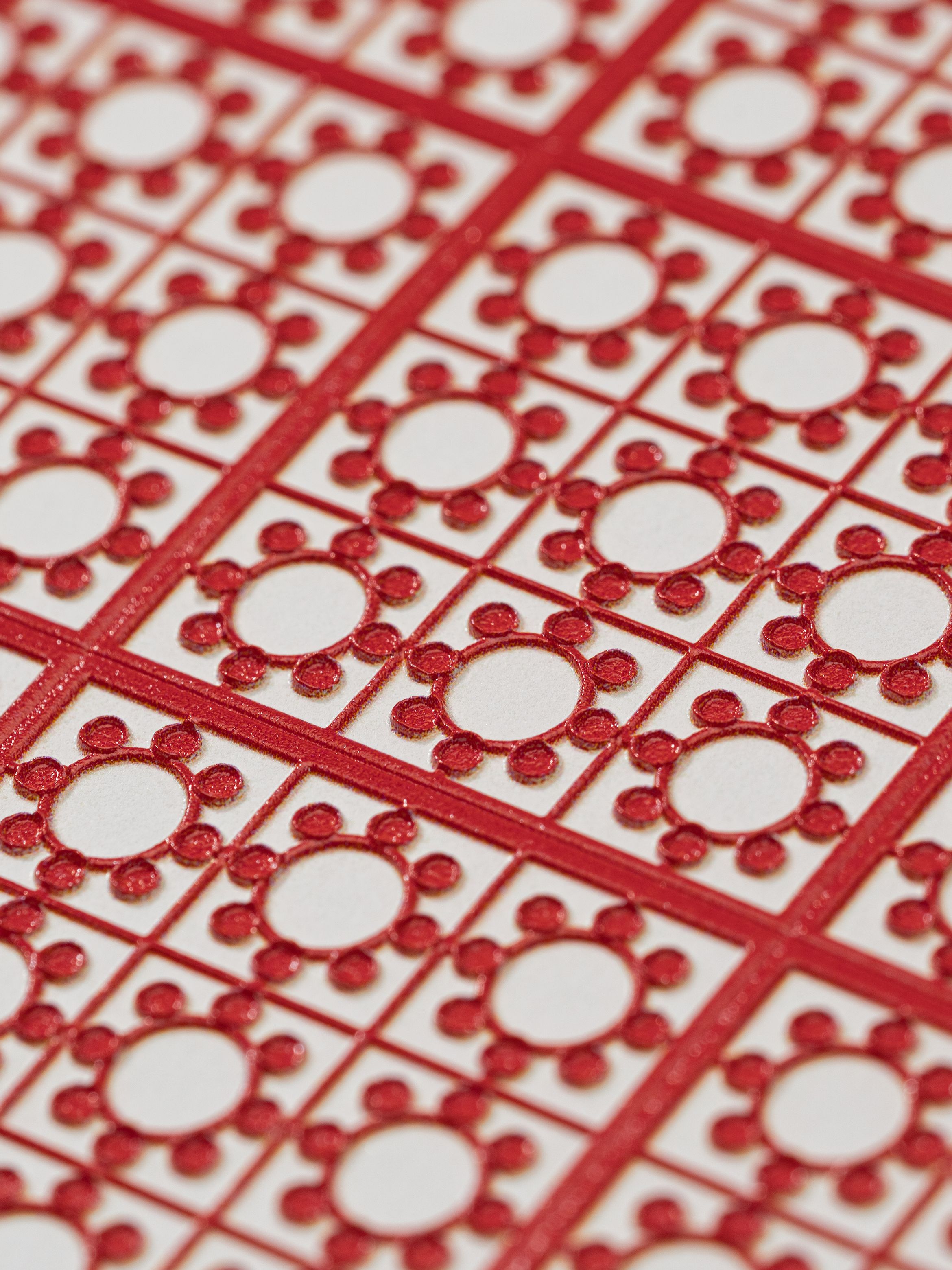 Red and white geometric pattern with circular and dot motifs in a grid arrangement on a textured surface.