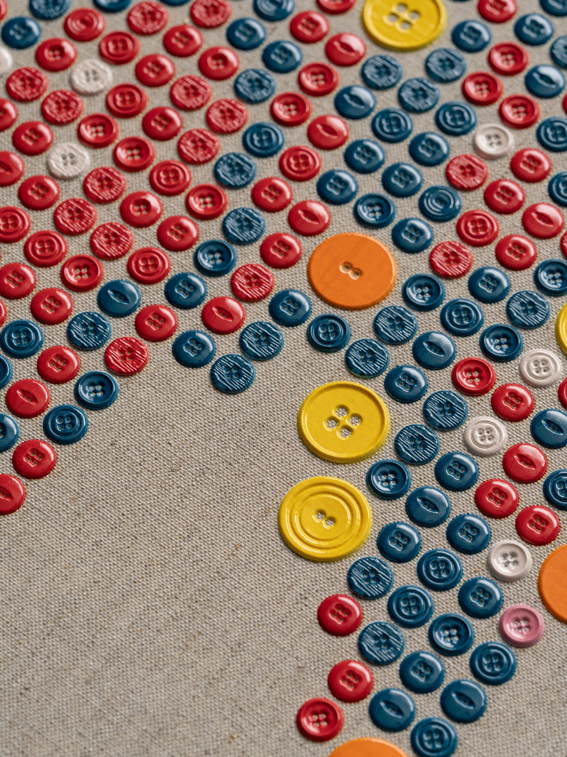 A collection of colorful buttons in red, blue, yellow, orange, and white, arranged in a pattern on a beige fabric background.