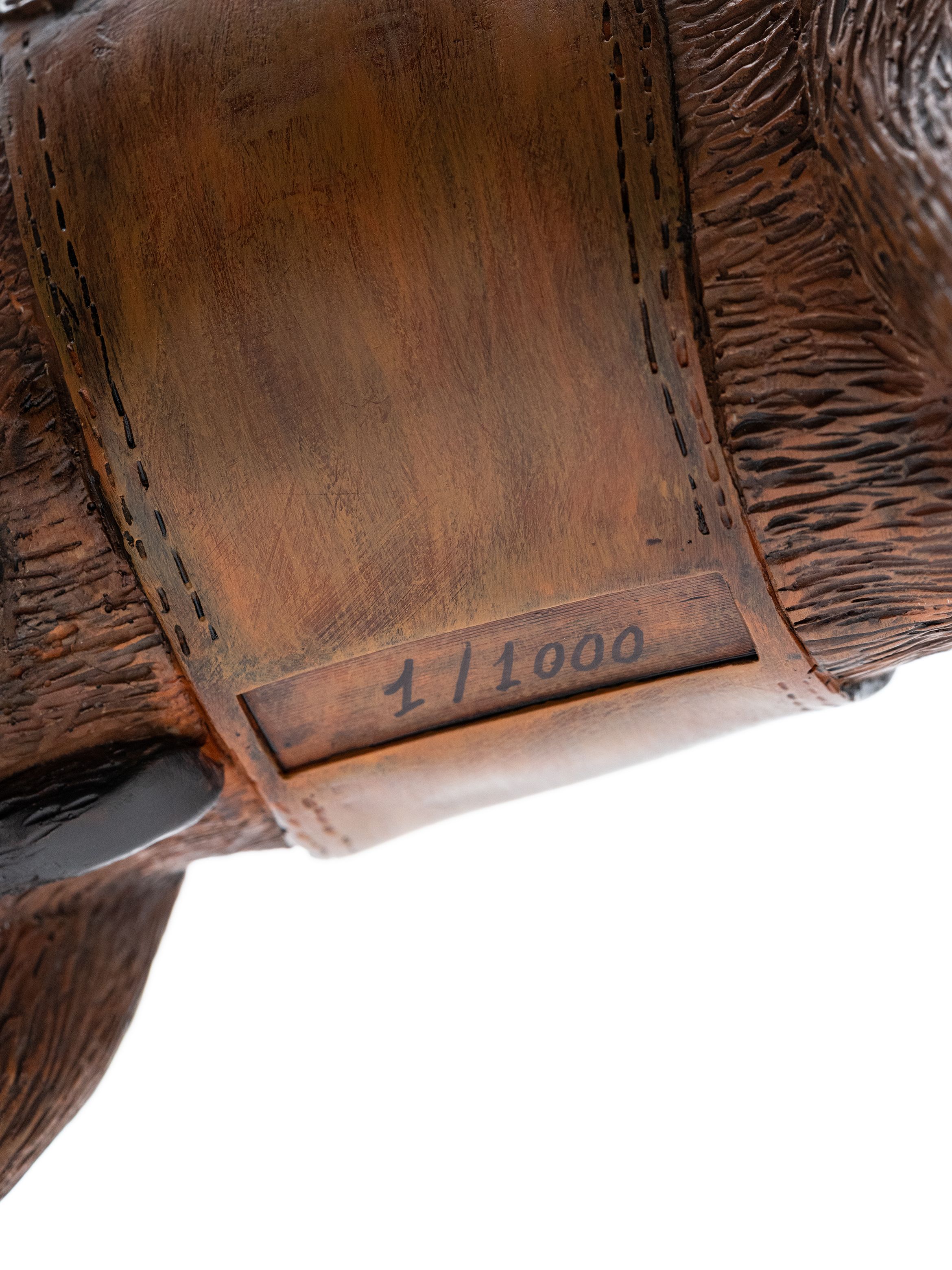 Close-up of an object with detailed carving and stitching patterns, featuring the numbering "1/1000" in black on a smooth, brown surface.