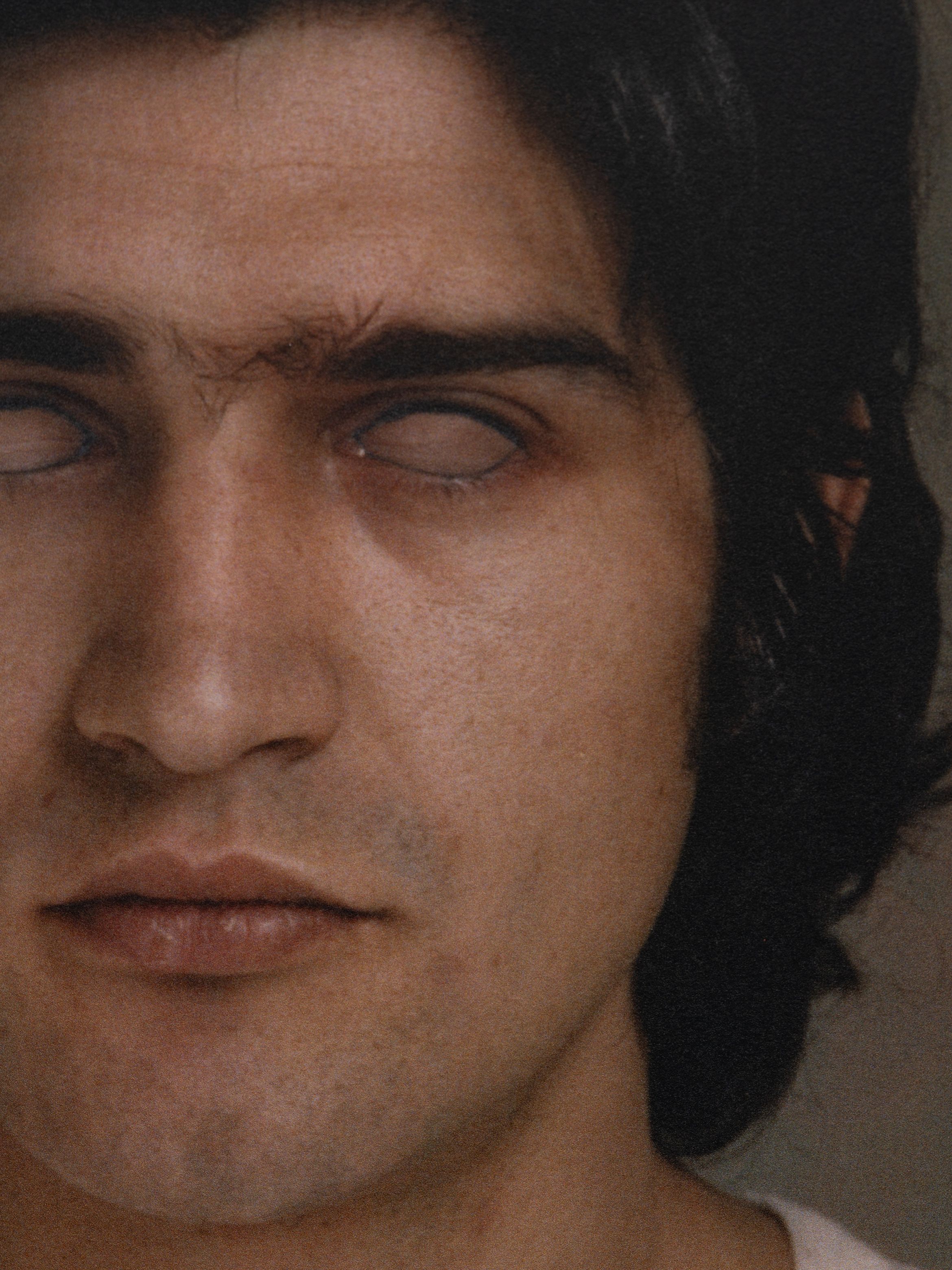 Close-up of a person with dark hair, eyes are white, and slightly parted lips, showing a calm facial expression.