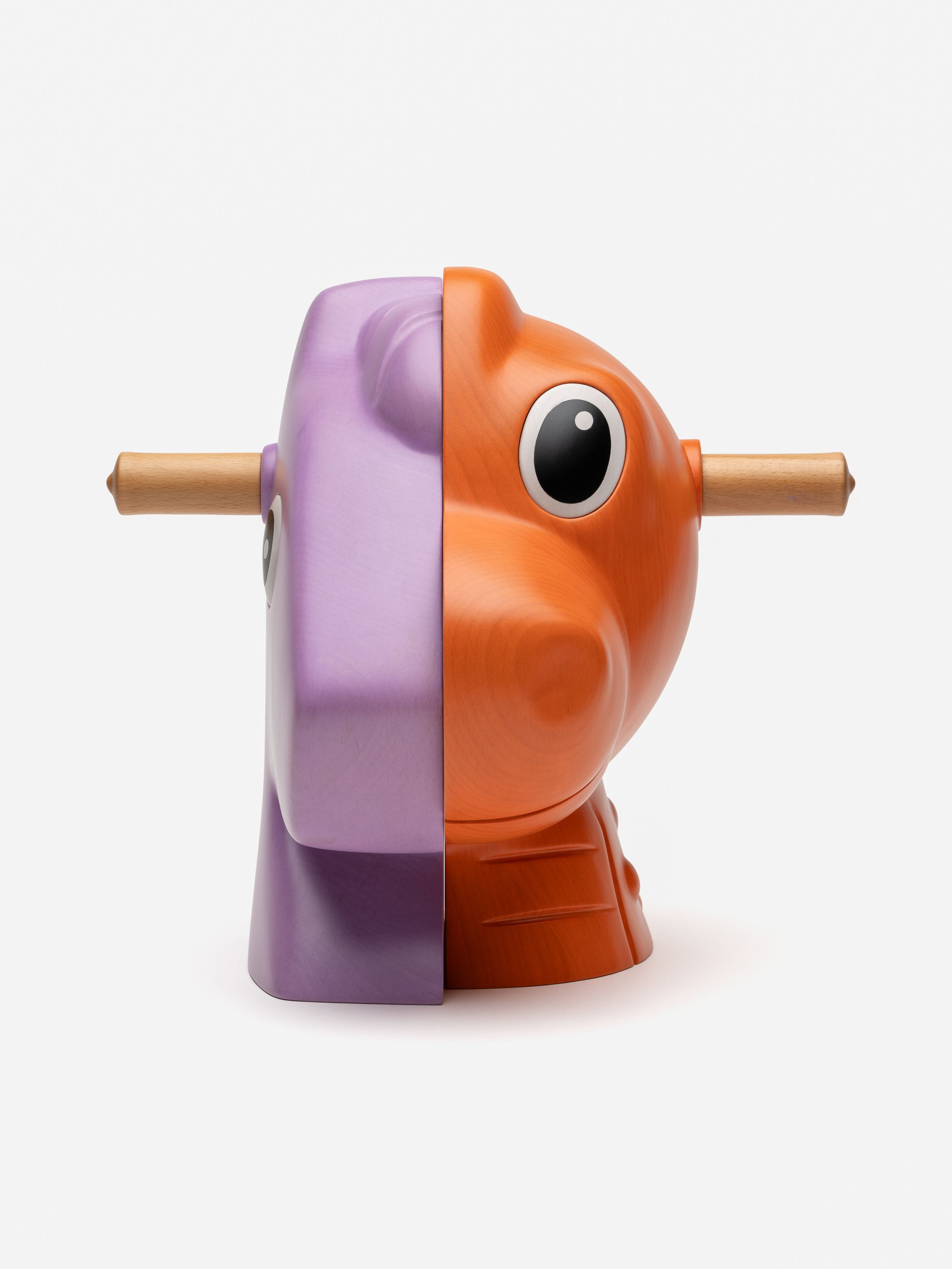 Wooden toy split in half; purple on left, orange on right, with large eyes and a rod through the center, on a white background.