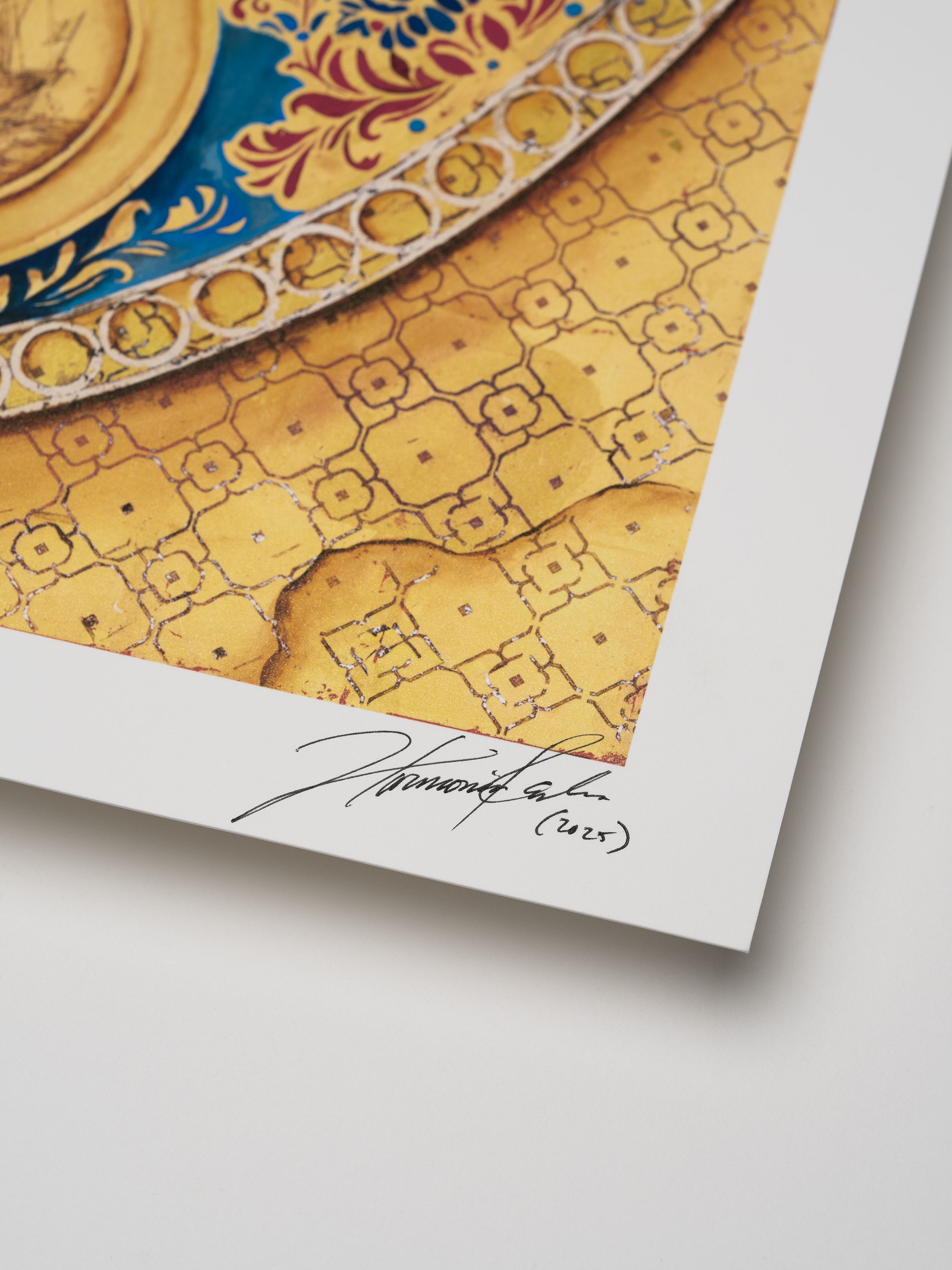Close-up of a signed artwork print featuring intricate yellow and blue patterns with a decorative border and a signature in black ink.