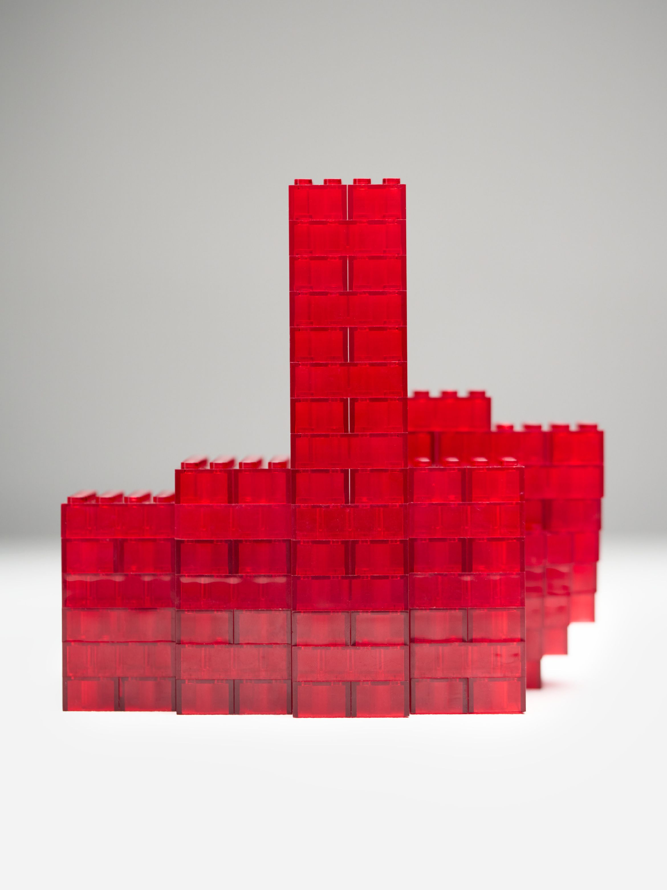Red translucent building blocks arranged in a structure with a tall central tower against a plain grey background.