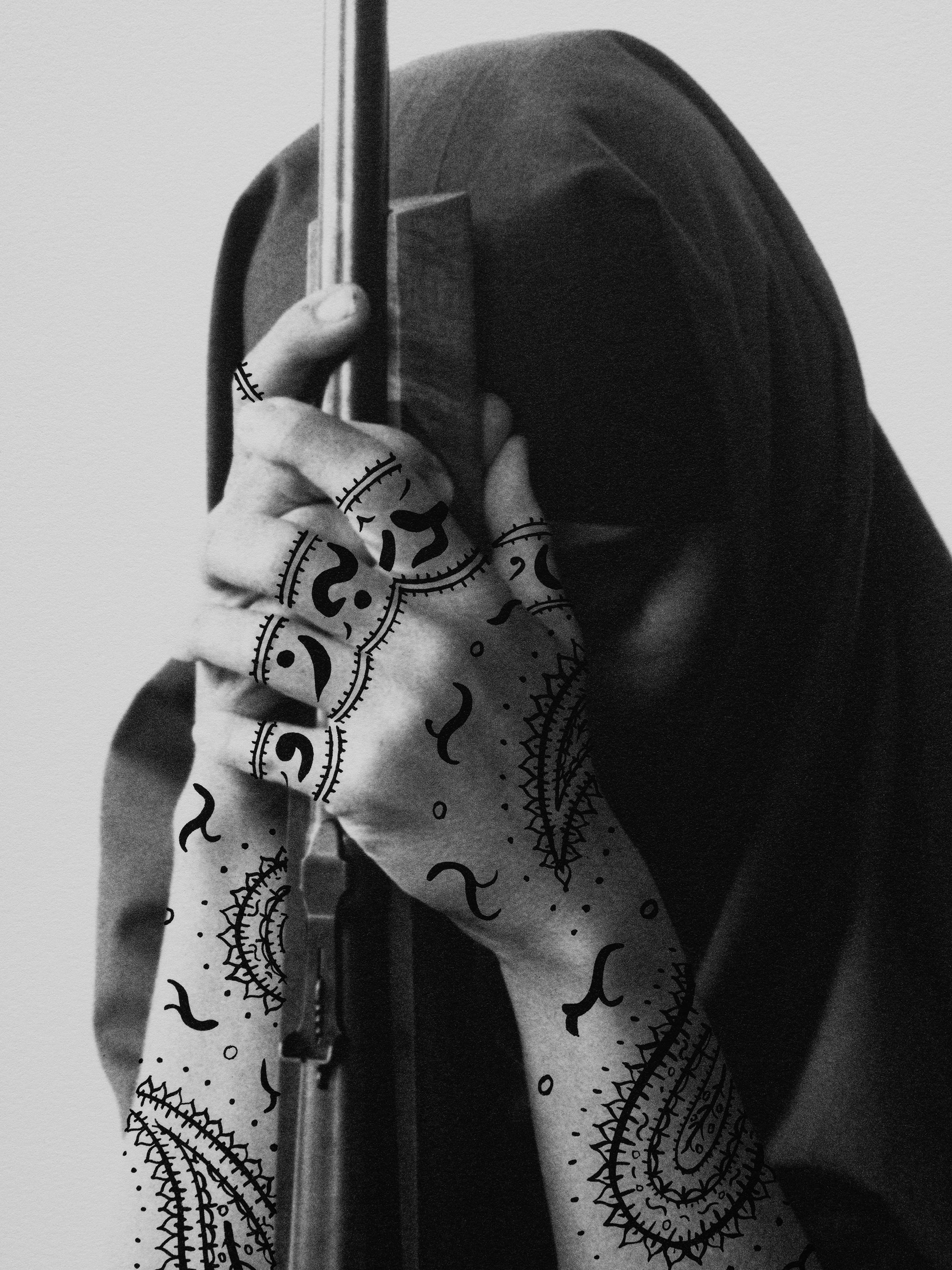 A person in a headscarf holds a rifle, hands adorned with intricate henna designs, against a plain background.