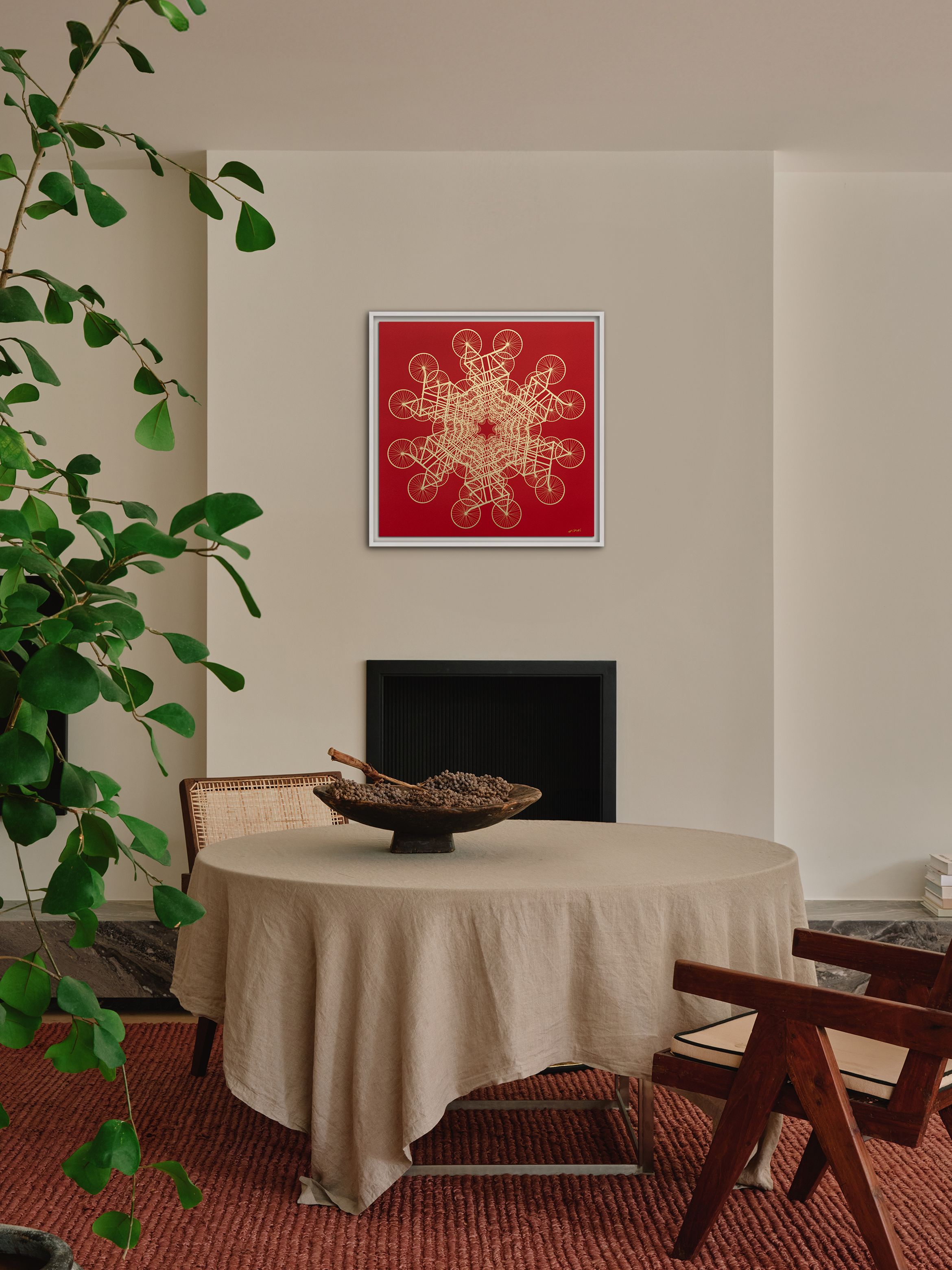 A cozy dining area with a round table covered in a beige cloth, wooden chairs, a potted plant, and red artwork on the wall above a fireplace.