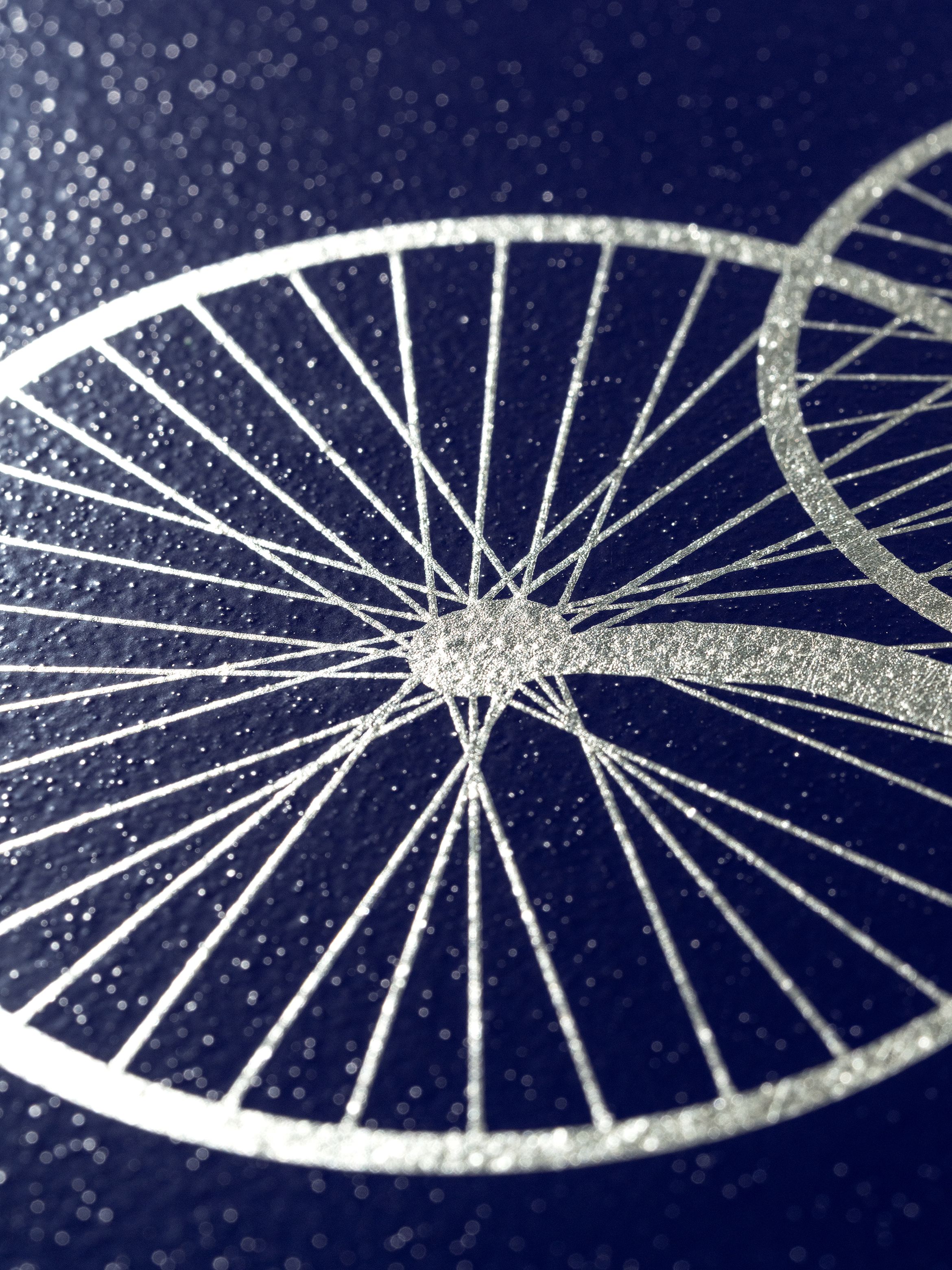 Close-up of a metallic bicycle wheel design on a dark, textured surface, highlighting the intricate spokes and circular patterns.