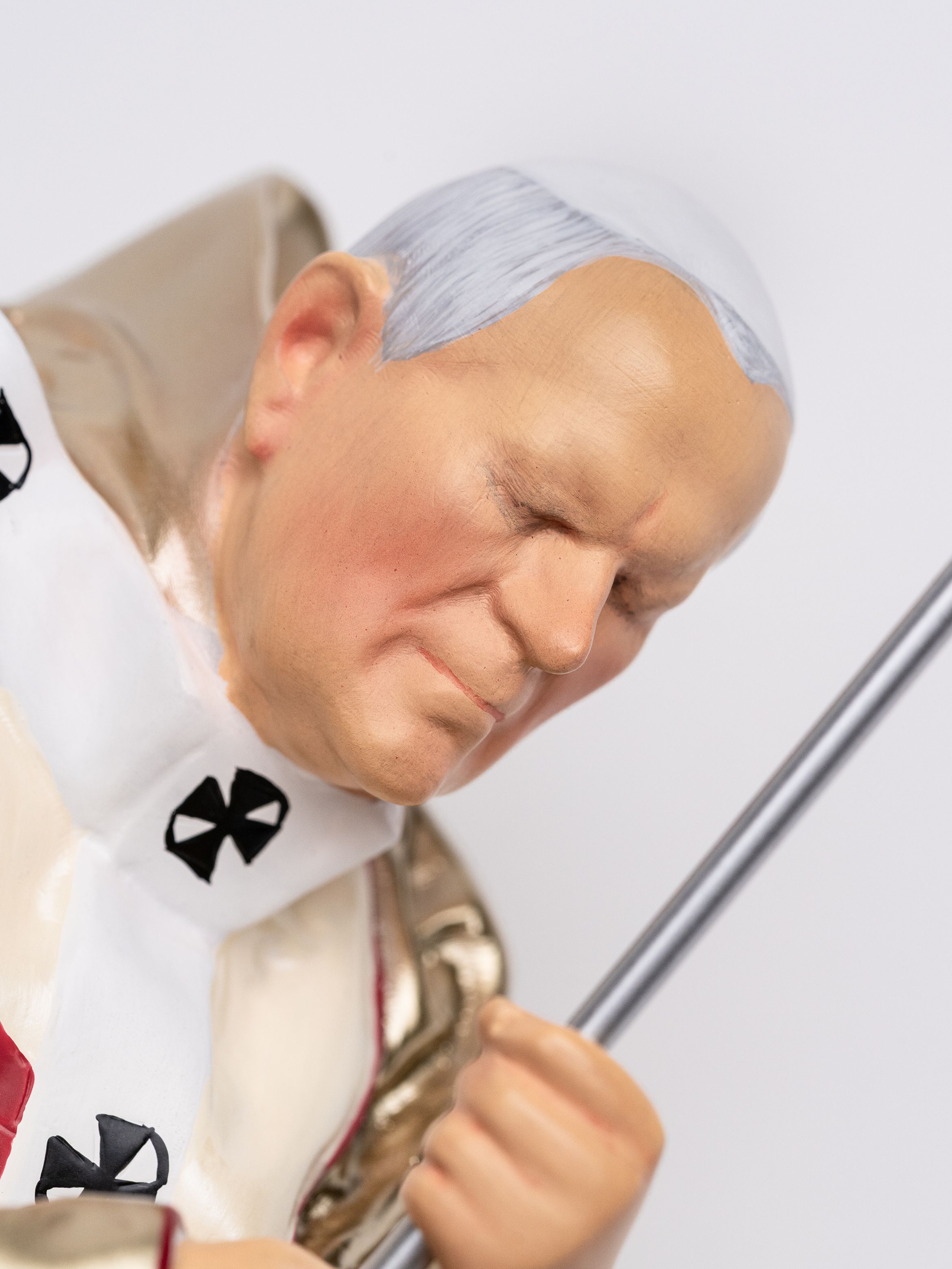A close-up of a statue depicting a religious figure with closed eyes, wearing a white robe with black crosses and holding a staff.