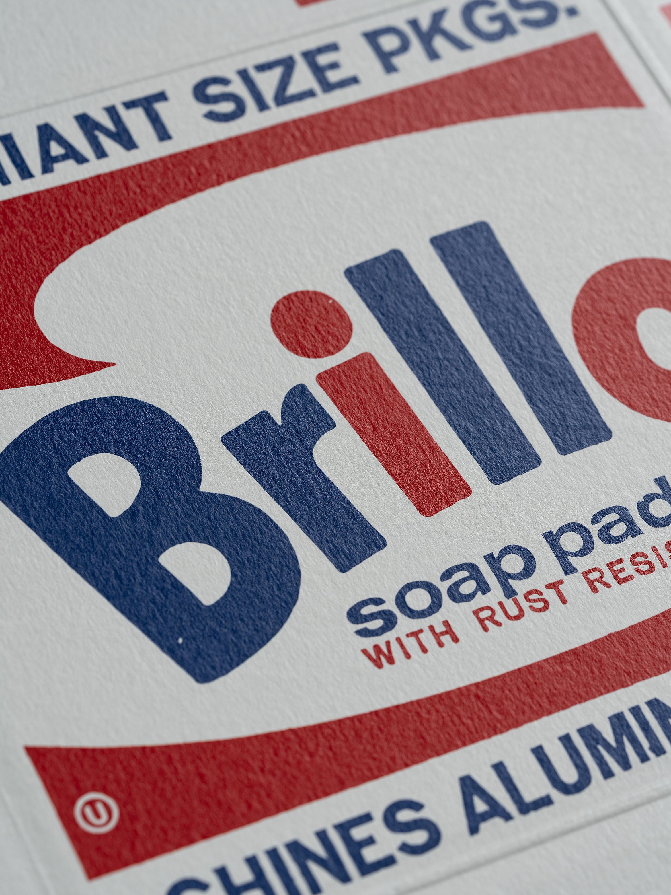 Close-up of Brillo soap pads packaging with red and blue text on a white background. Keywords include "GIANT SIZE PKGS" and "SHINES ALUMINUM."