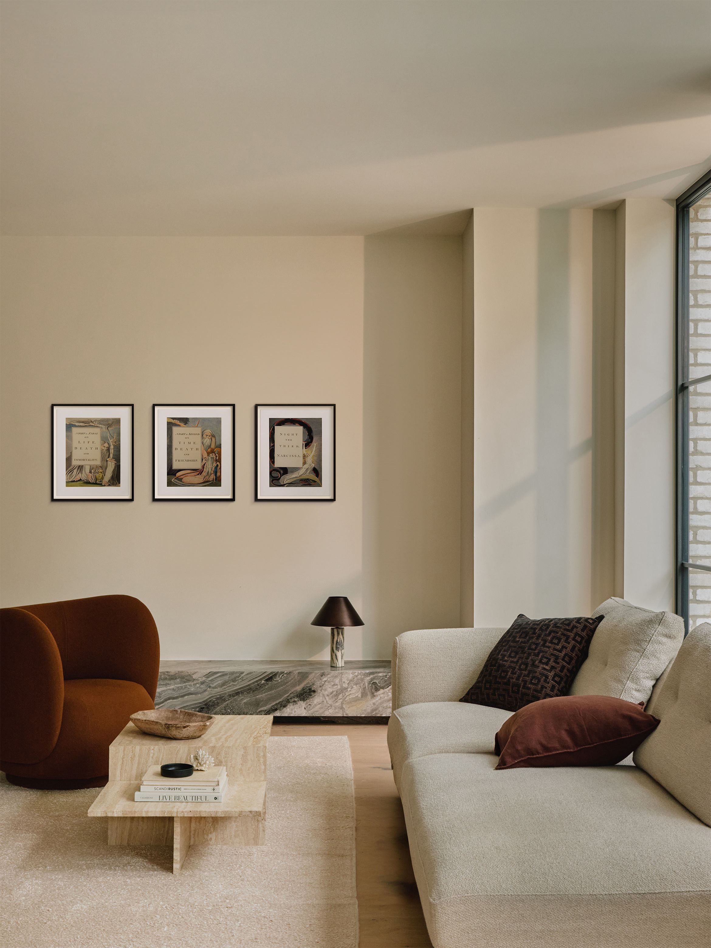 Modern living room with beige sofa, brown chair, marble coffee table, and framed art on the wall. Large window lets in natural light.