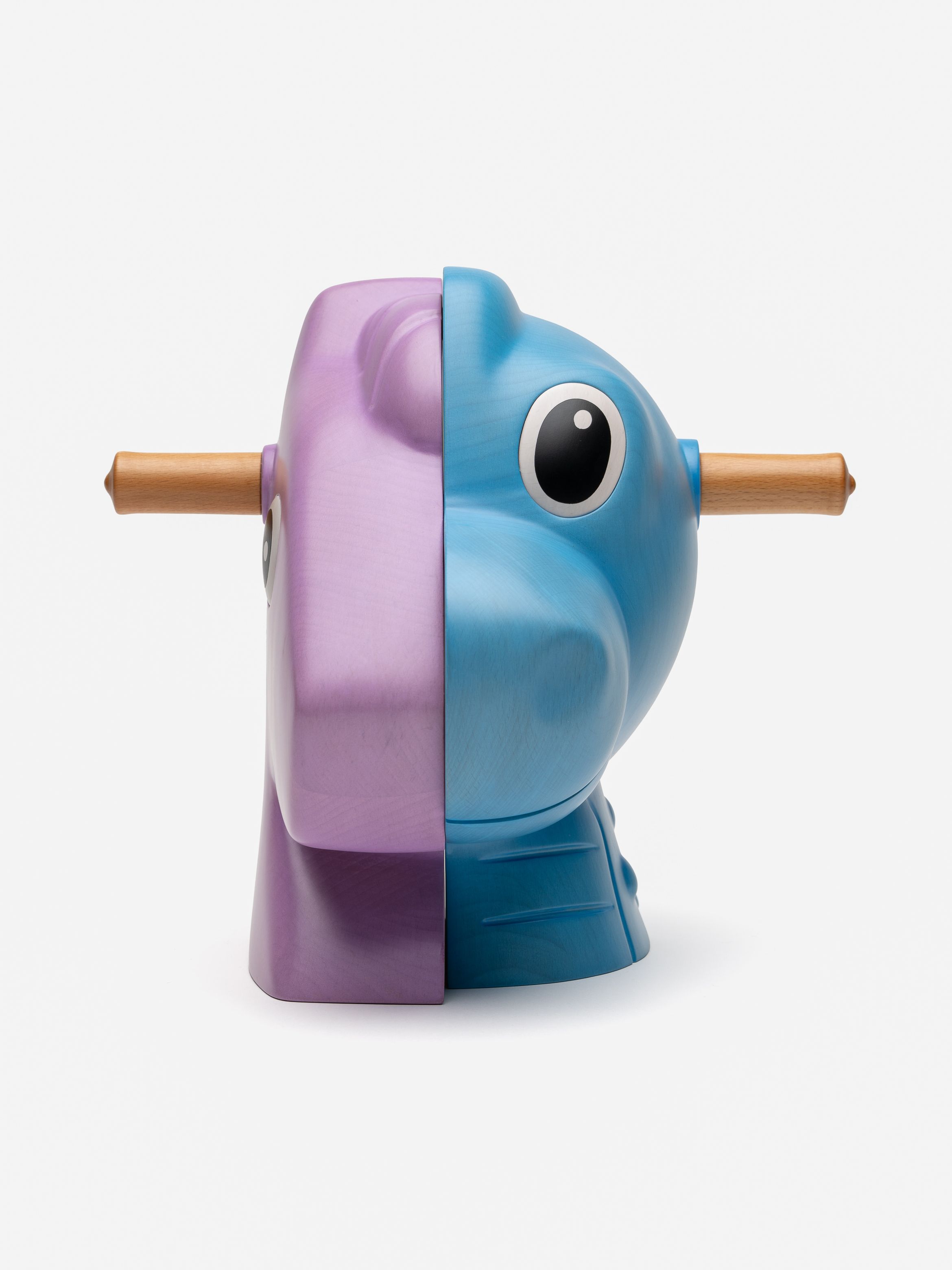 Wooden toy split in half; pink on left, blue on right, with large eyes and a rod through the center, on a white background.