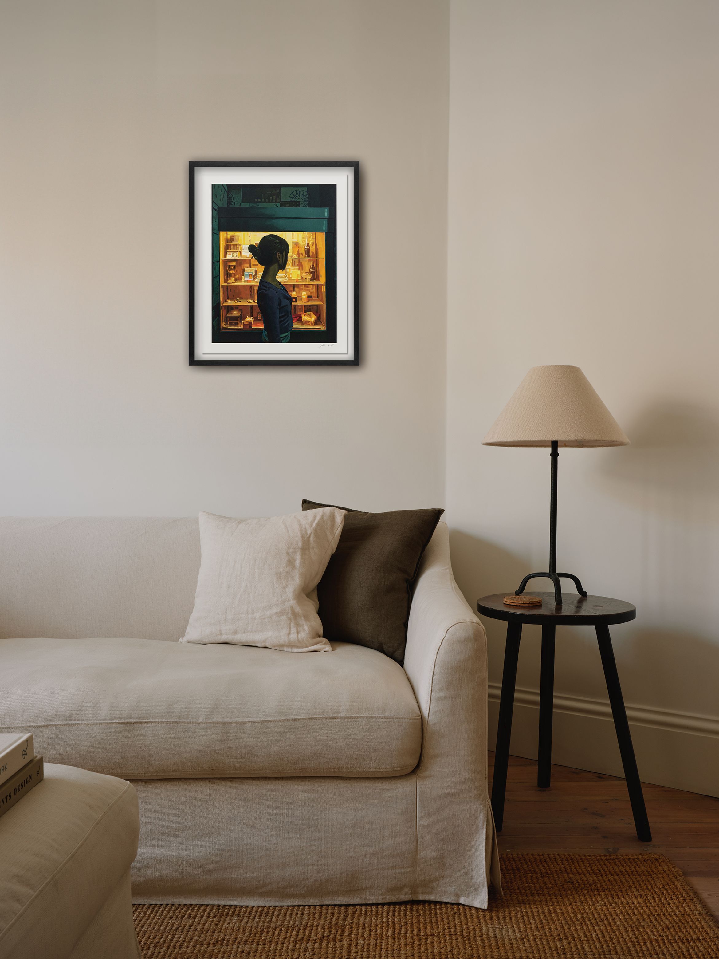 Minimalist living room with a white sofa, cushions, a side table with a lamp, and a framed silhouette artwork on the wall.