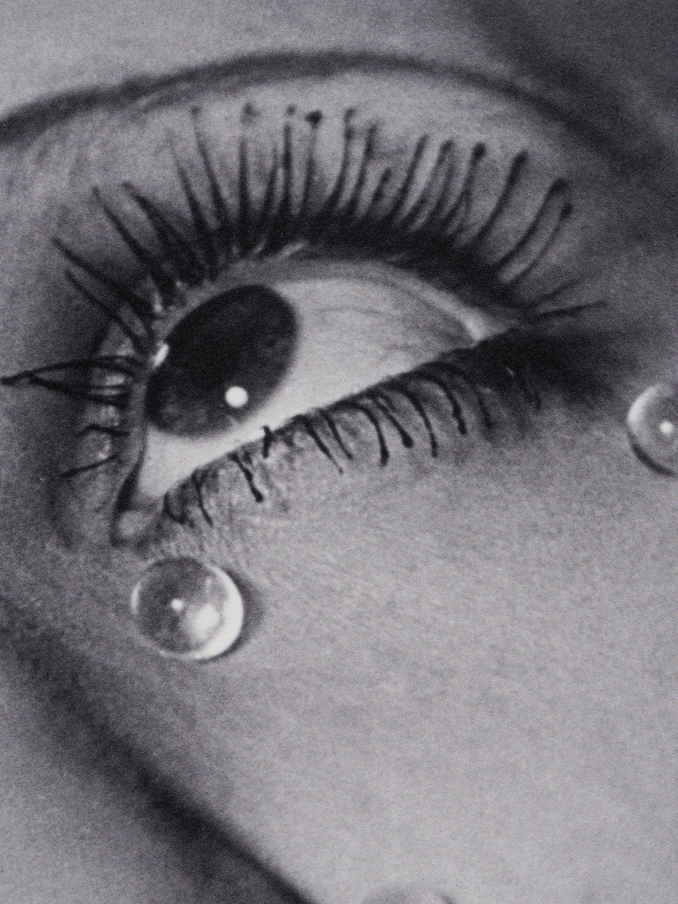 Grainy black-and-white close-up of an eye with long lashes and glassy spherical teardrops on the cheek.