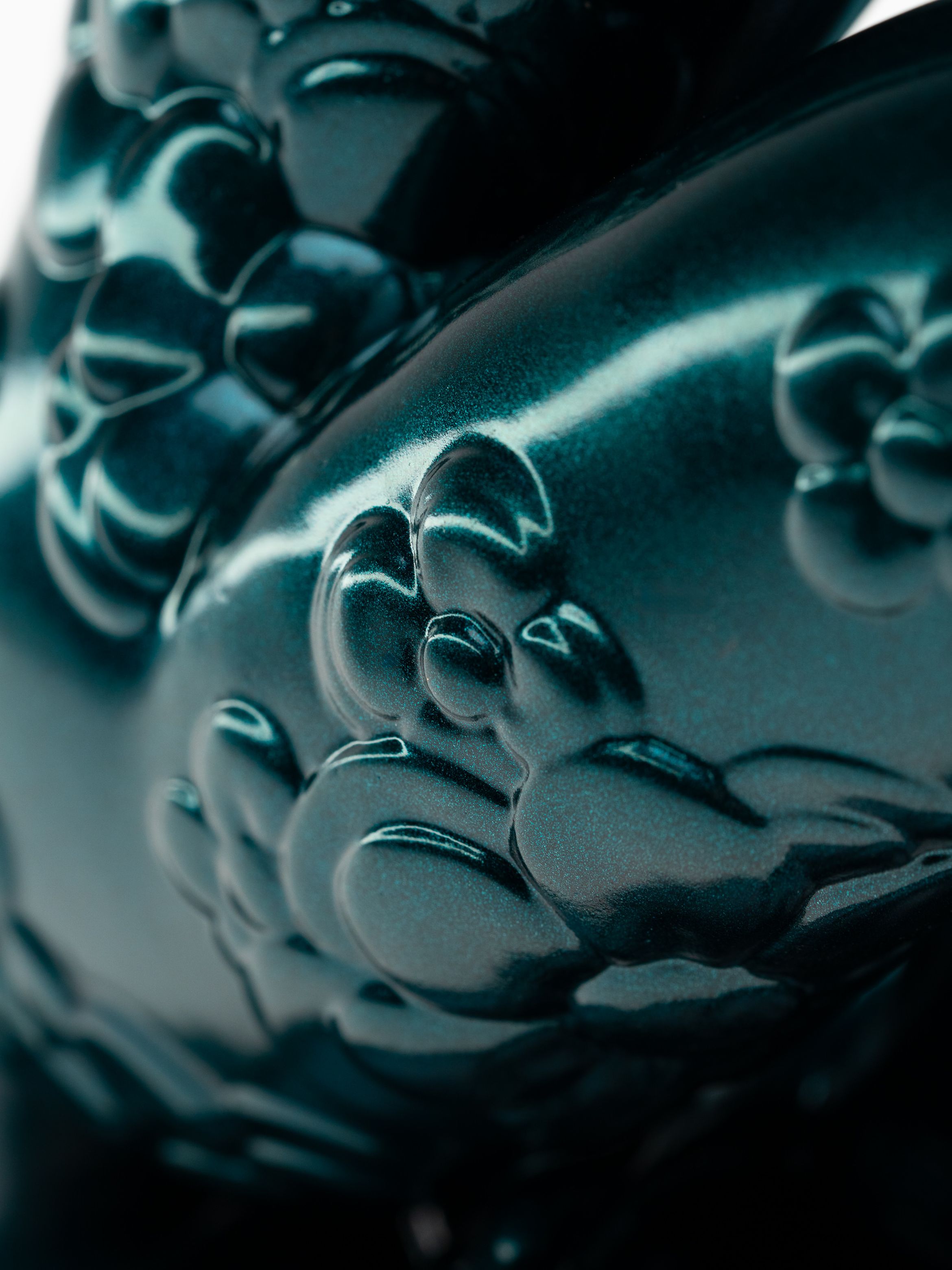 Close-up of a metallic sculpture with intricate floral patterns, depicting a seated figure on a flower-shaped base.