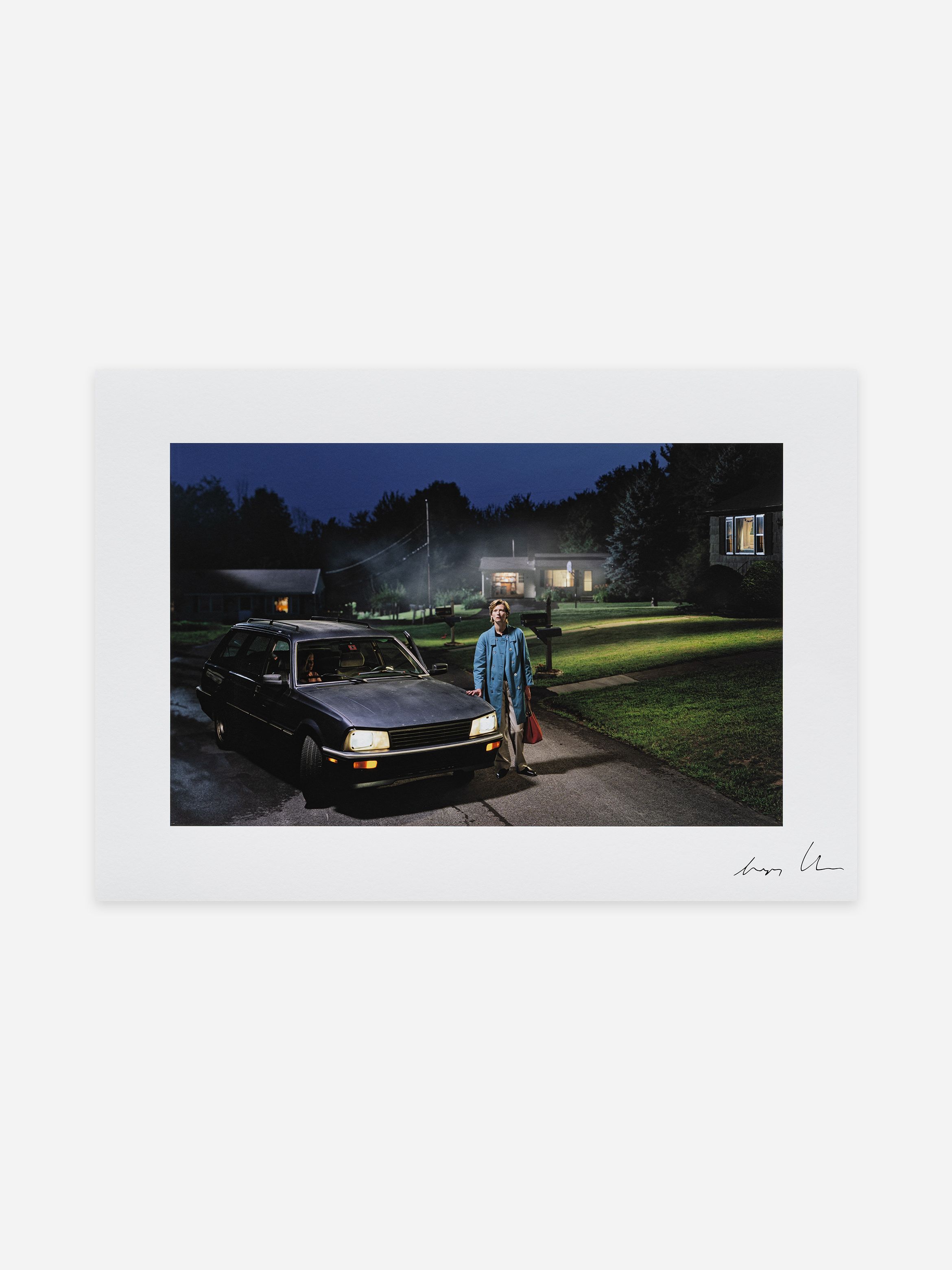 Person in blue coat with a bag stands beside a parked car on a dimly lit suburban street at night, with houses visible in the background. Person in blue coat with a bag stands beside a parked car on a dimly lit suburban street at night, with houses visible in the background.