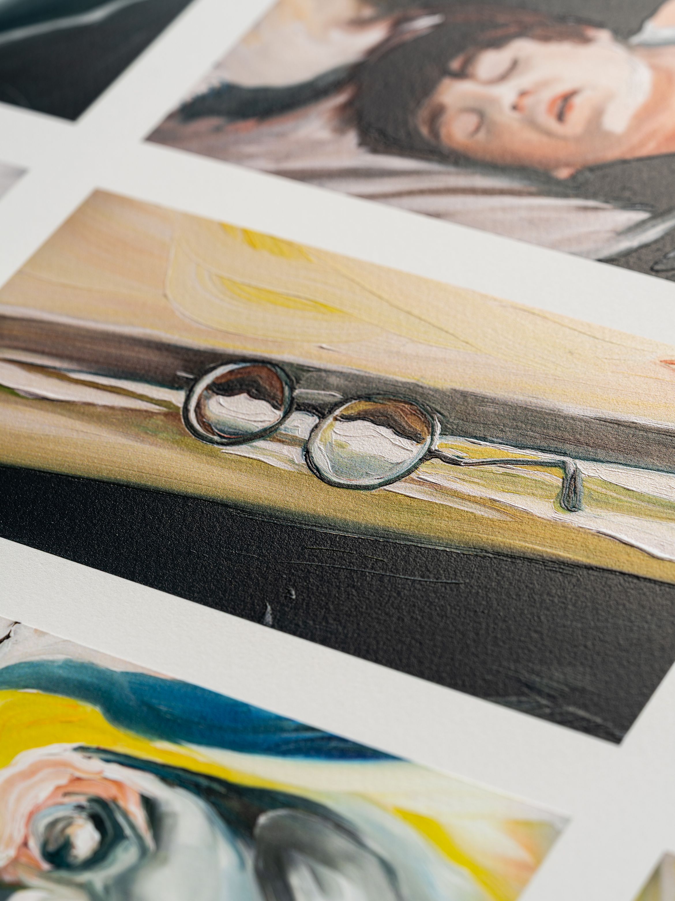 Close-up of an art print featuring round glasses on a surface with soft, abstract colours. Other blurred artwork images visible around it.