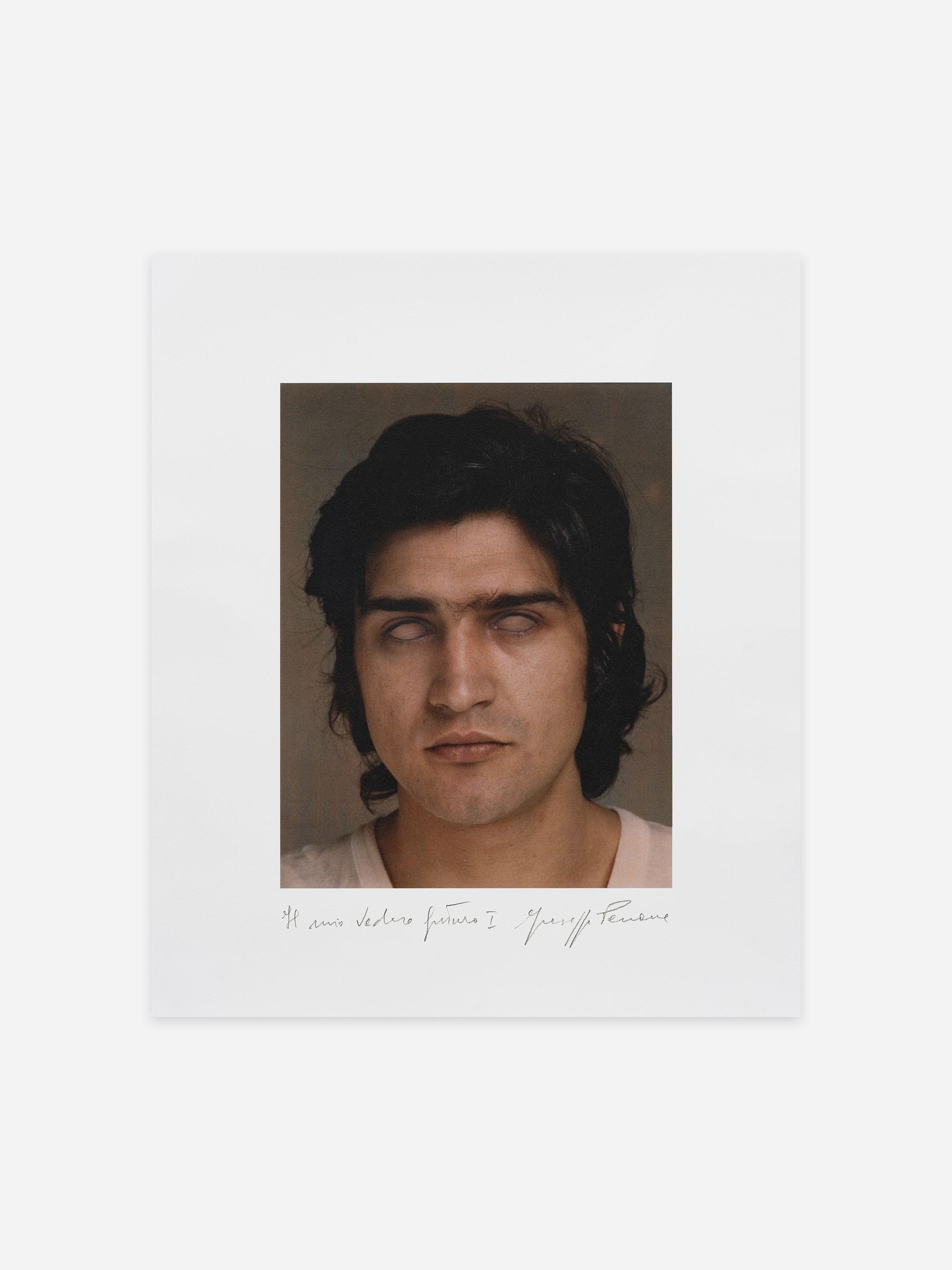 A portrait of a person with dark hair, eyes open but white, and a neutral expression, set against a plain background. Handwritten text below the image.