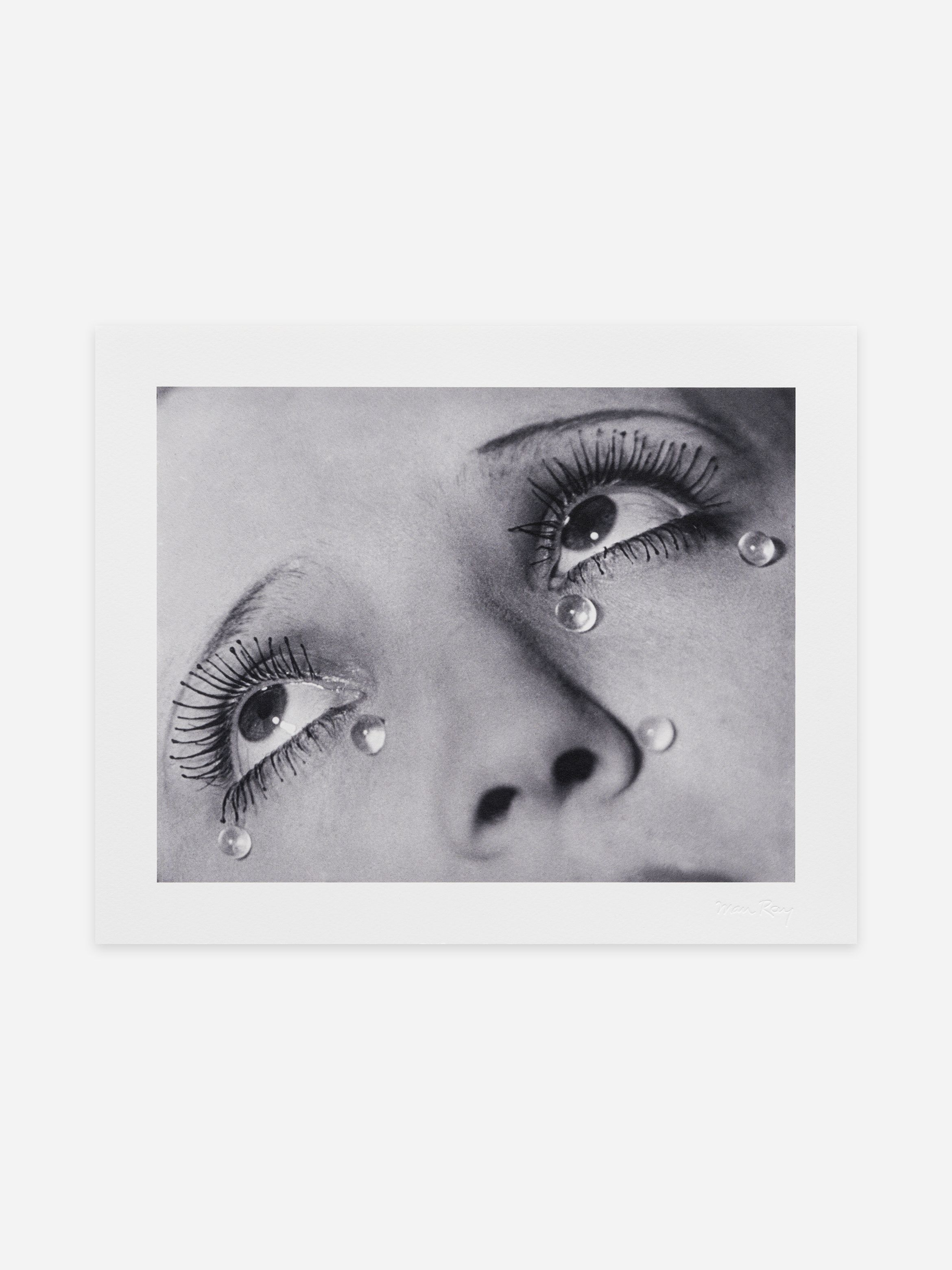Black-and-white close-up of a woman's face, eyes looking upward with long lashes and glass teardrops adhered beneath her eyes.