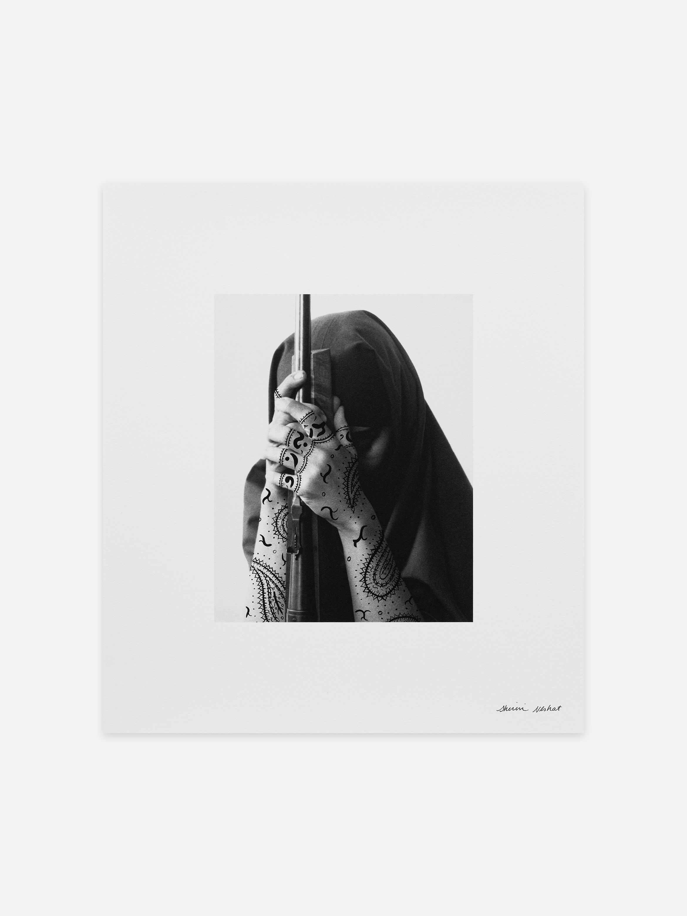 Black and white photo of a person with a covered head, holding a rifle. Their hands are adorned with intricate henna designs.