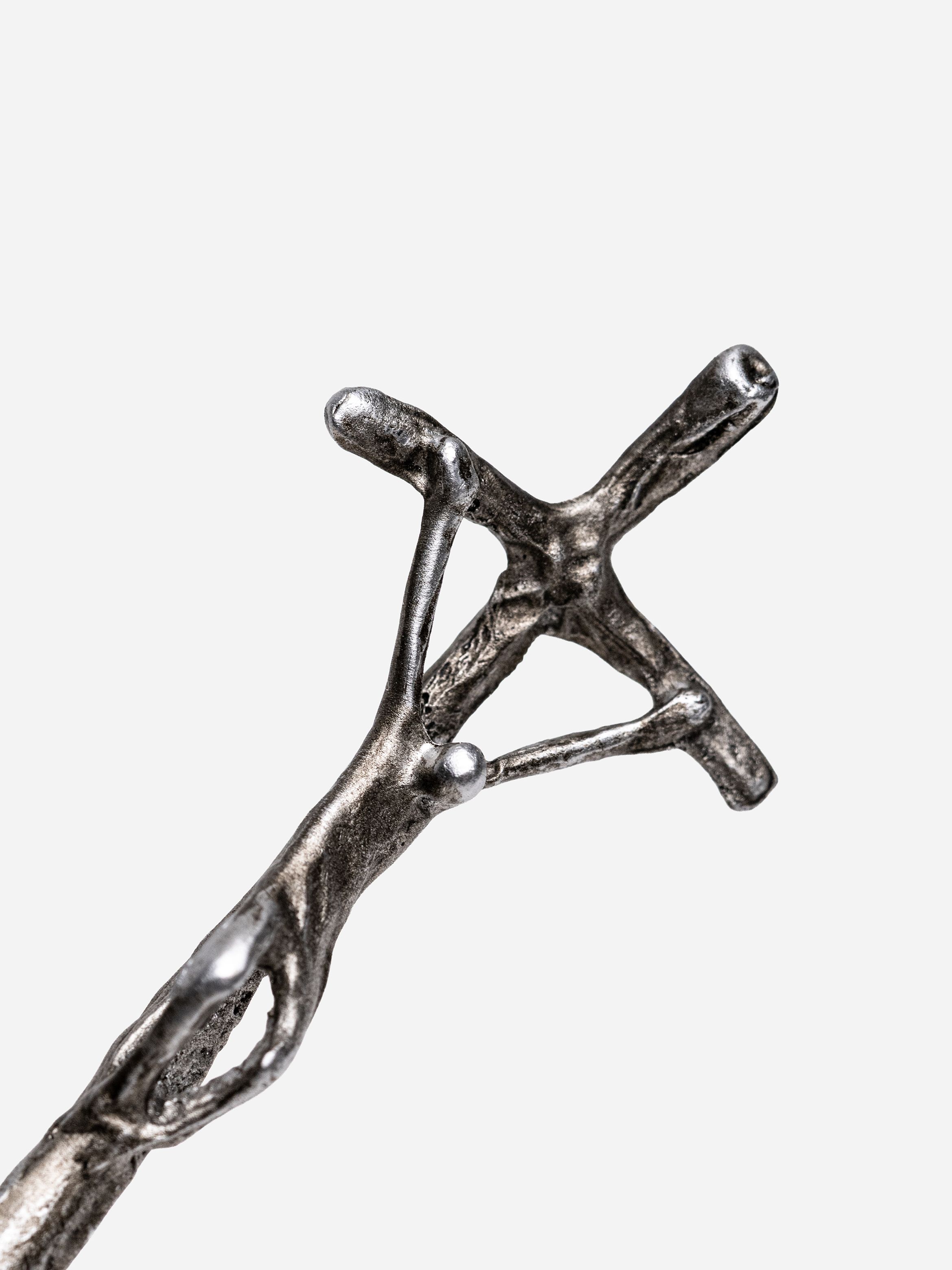 Close-up of a metallic abstract sculpture depicting a figure on a cross.