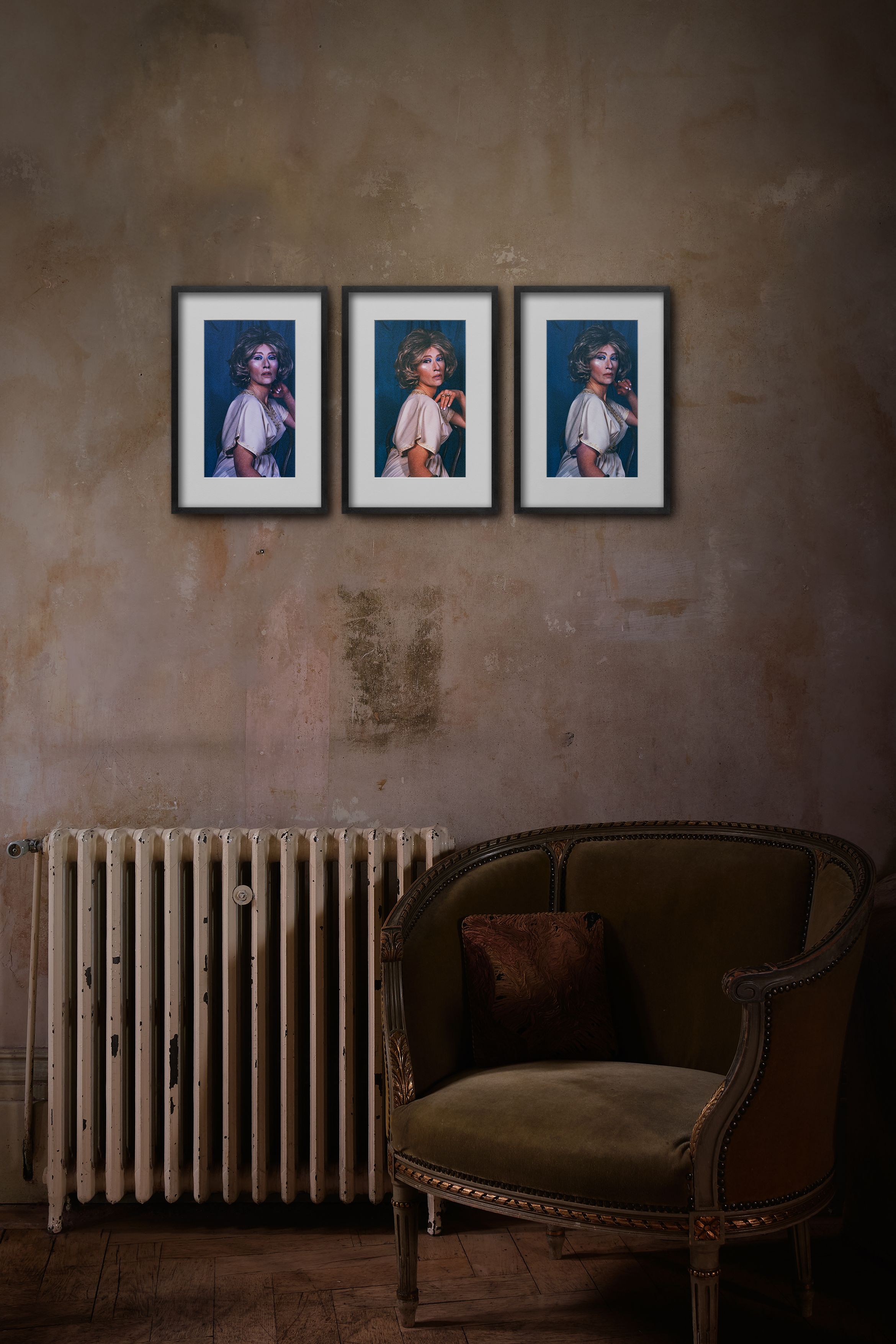 Three framed portraits of a woman hang above a vintage radiator and an upholstered armchair in a dimly lit room with textured walls.