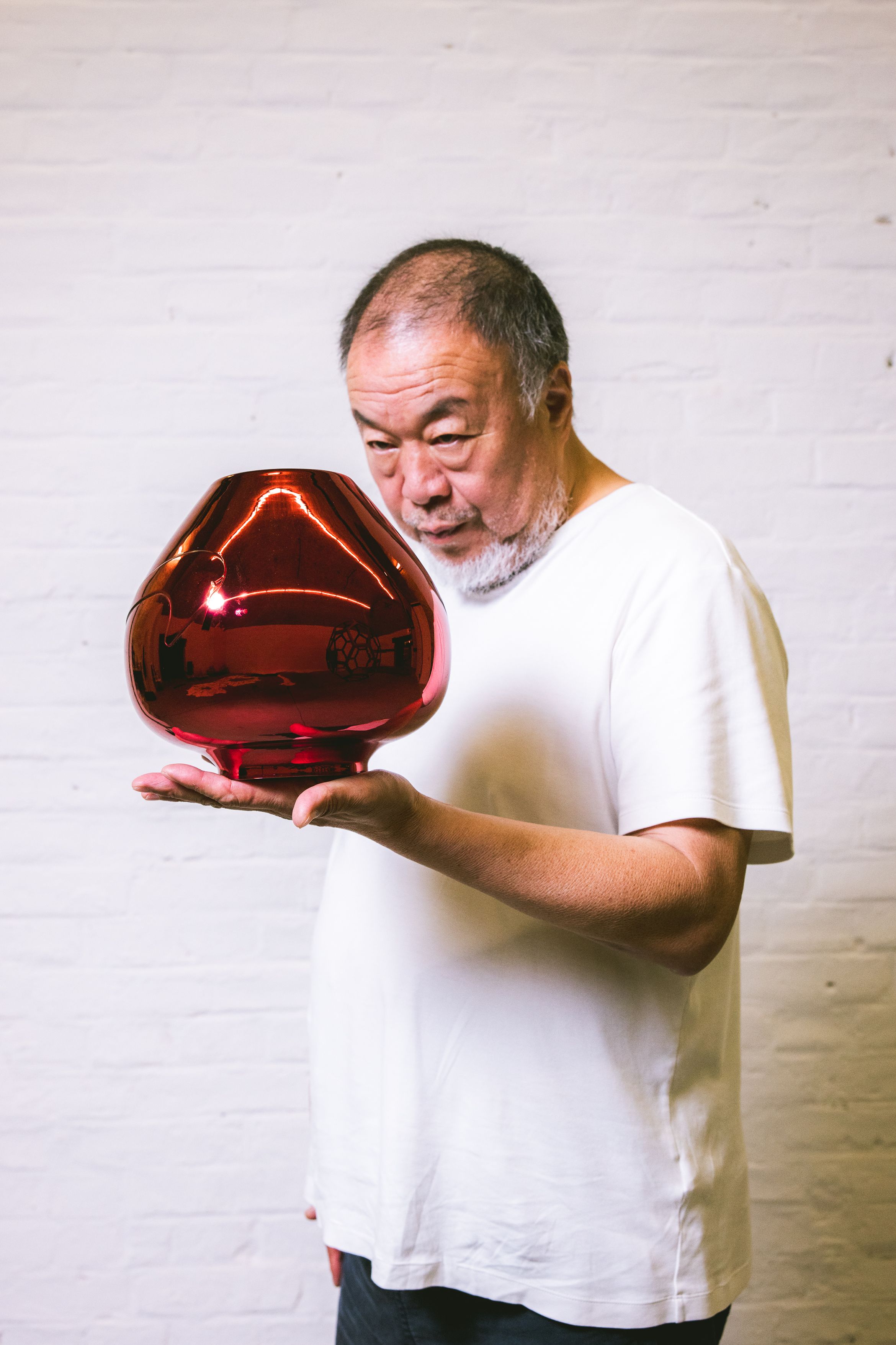 An image of artist Ai Weiwei holding a coloured metal vase sculpture.