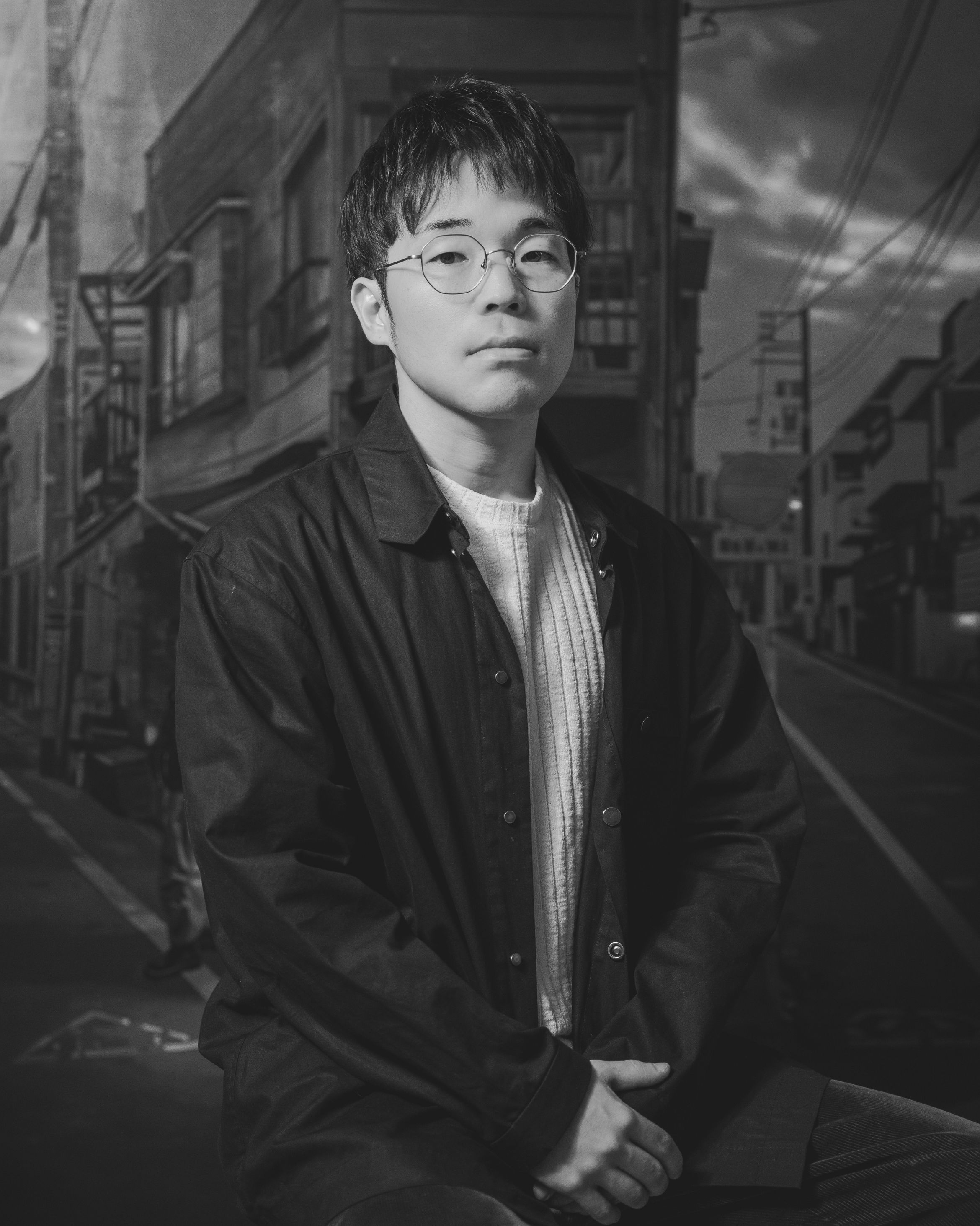 An image of artist Keita Morimoto, stood in front of one of his paintings – the image is in black and white.