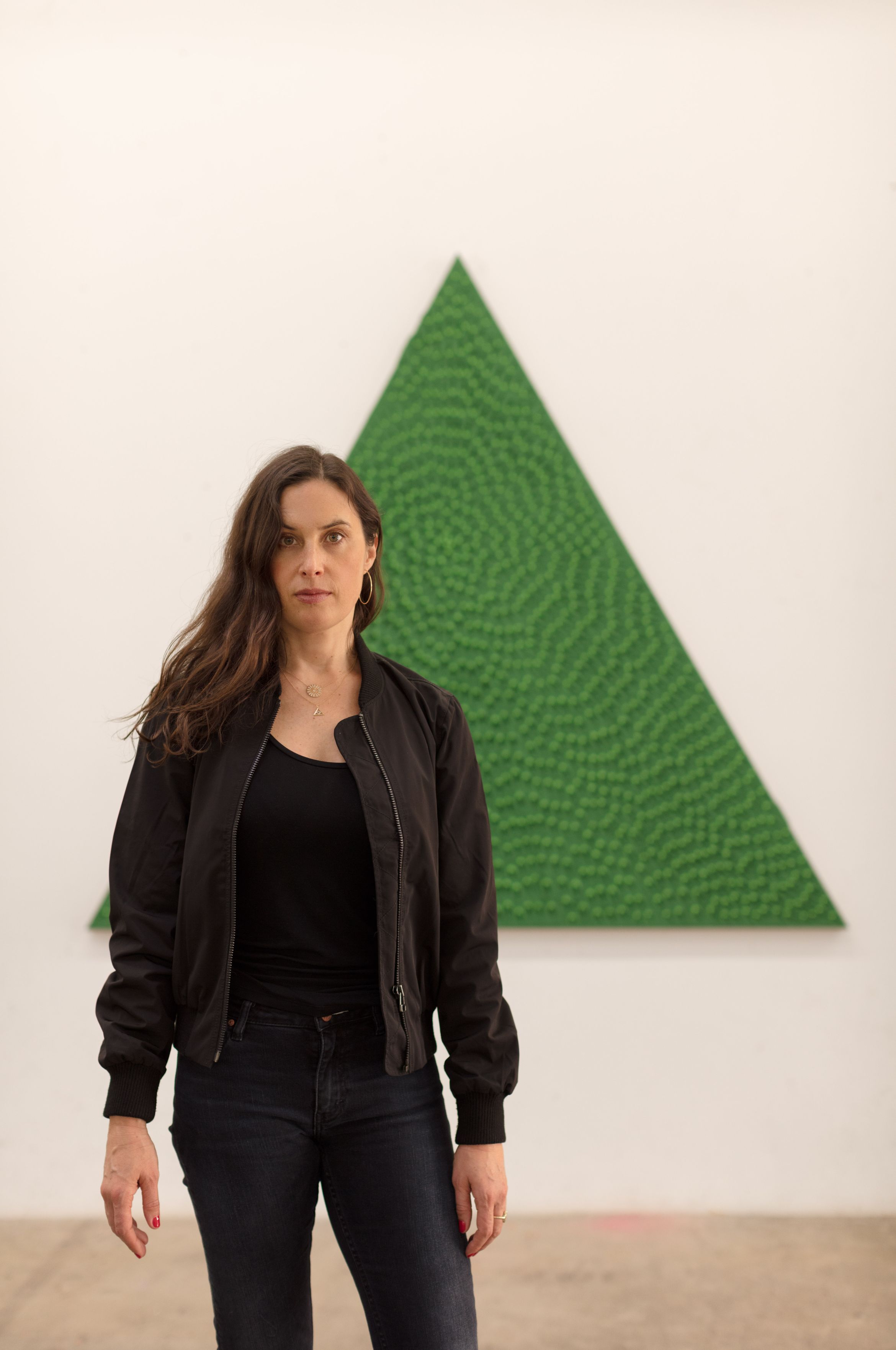 A person in a black jacket stands in front of a wall with a large, textured green triangle.
