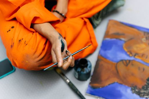 Artist sitting cross-legged on the floor holding a paintbrush dipped in black paint with a painting in front of her Artist sitting cross-legged on the floor holding a paintbrush dipped in black paint with a painting in front of her