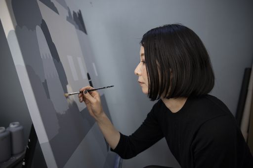 artist holding a paintbrush up to her canvas as she touches up some areas of grey artist holding a paintbrush up to her canvas as she touches up some areas of grey