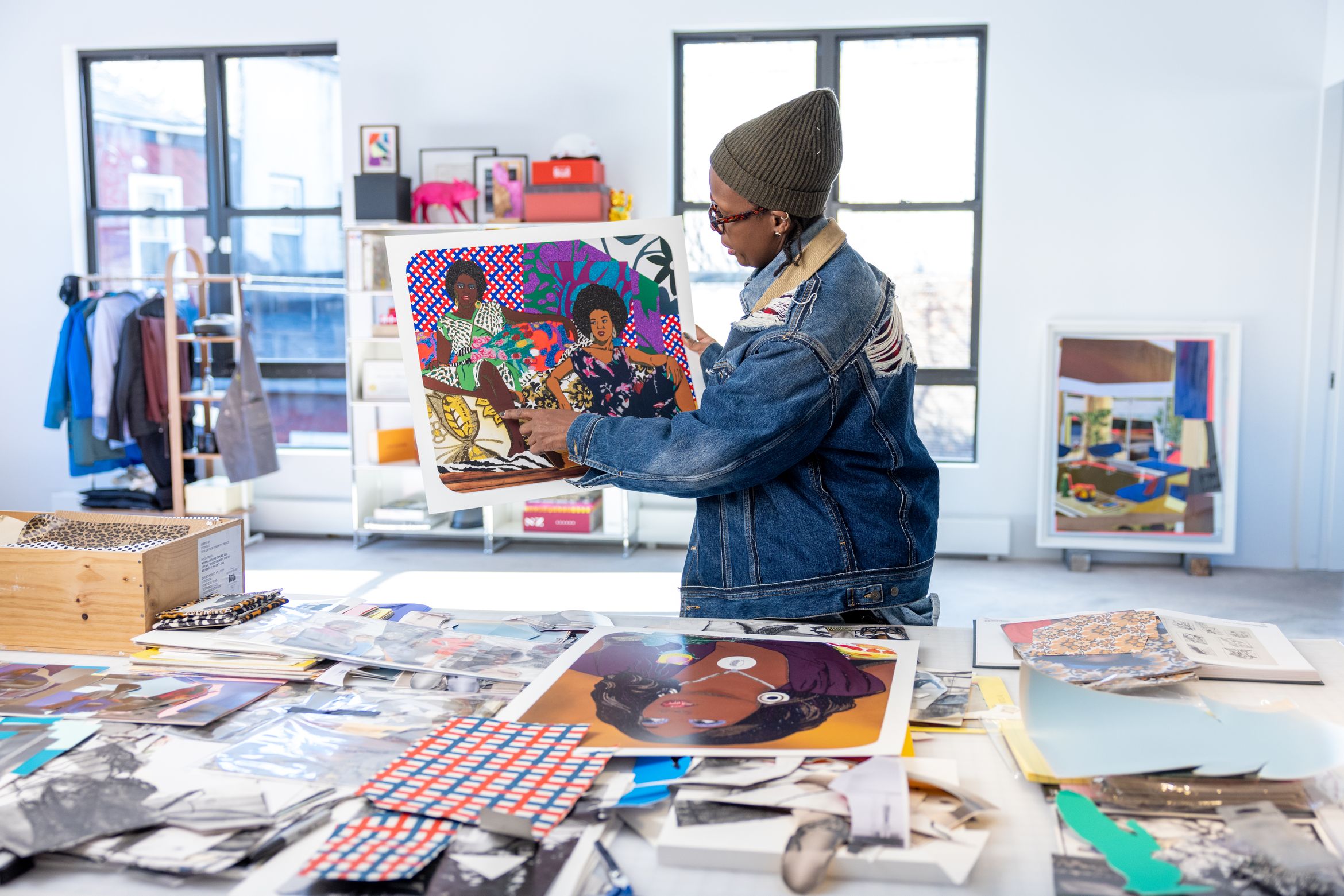An image of an artist in her studio, holding up a print and pointing to its detail.