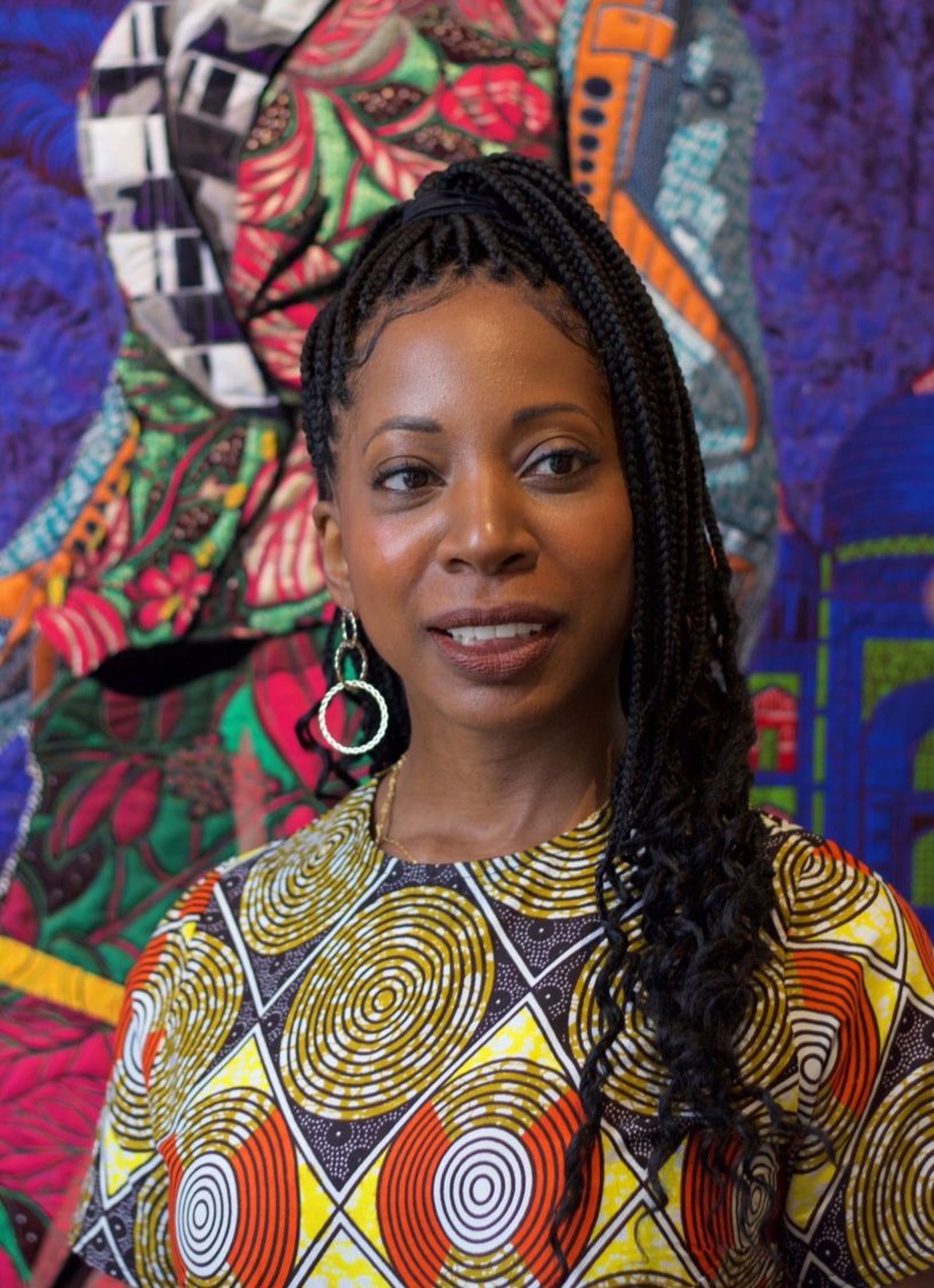 Artist Bisa Butler stands in front of a vibrant, patterned textile backdrop.