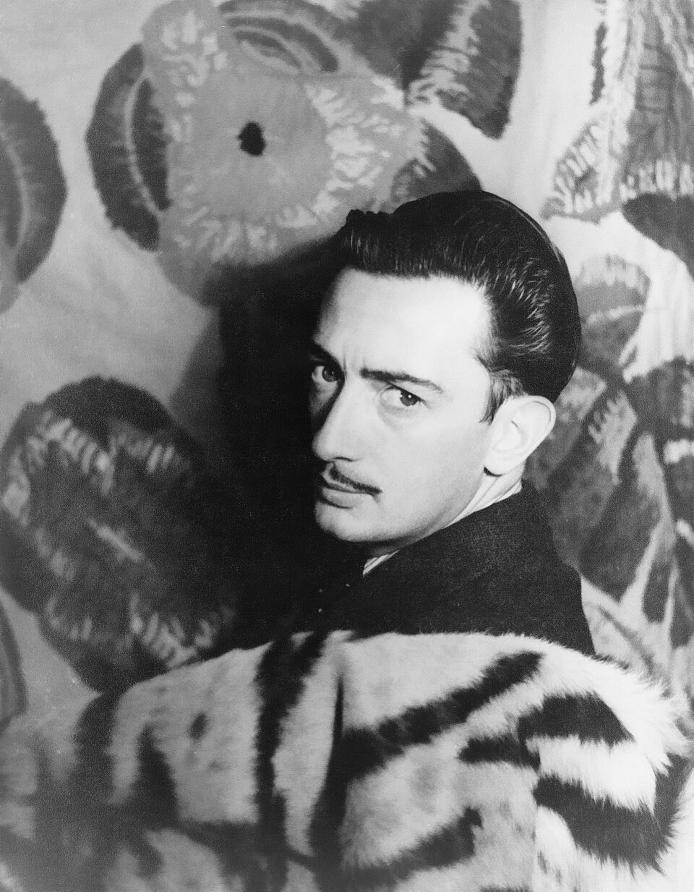 Black and white portrait of a man (Dali) with slicked-back hair and mustache, wearing a tiger-patterned coat against a floral backdrop.