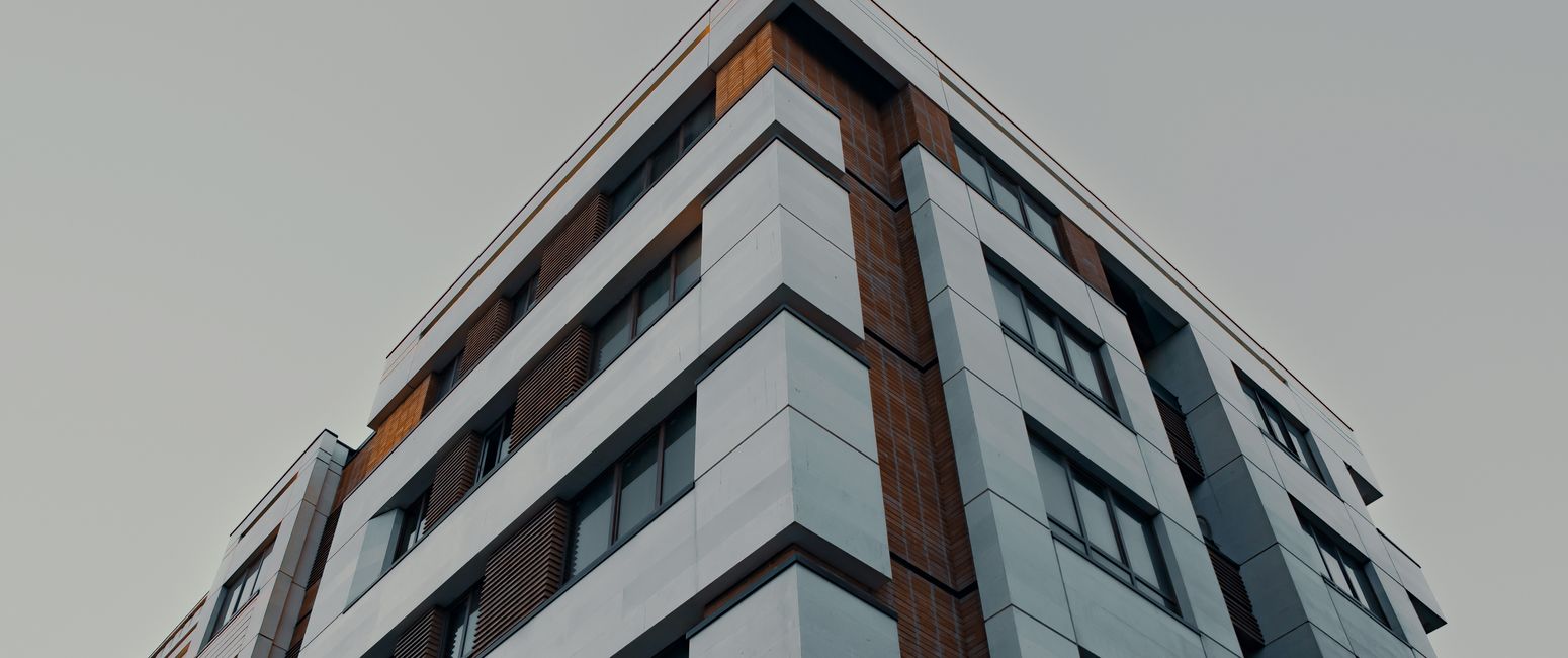 Low-angle view of a modern apartment building with a combination of gray and brown panels against a clear sky.
