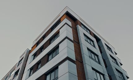 Low-angle view of a modern apartment building with a combination of gray and brown panels against a clear sky.