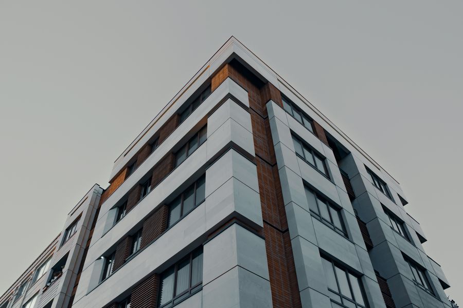 Low-angle view of a modern apartment building with a combination of gray and brown panels against a clear sky.