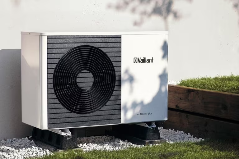 Outdoor heat pump unit on a gravel bed beside a grassy area, with a branded logo on the side.
