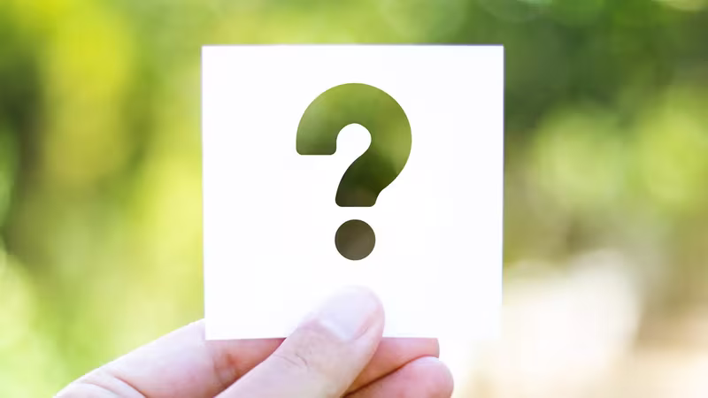 Hand holding a question-mark card against a blurred green background