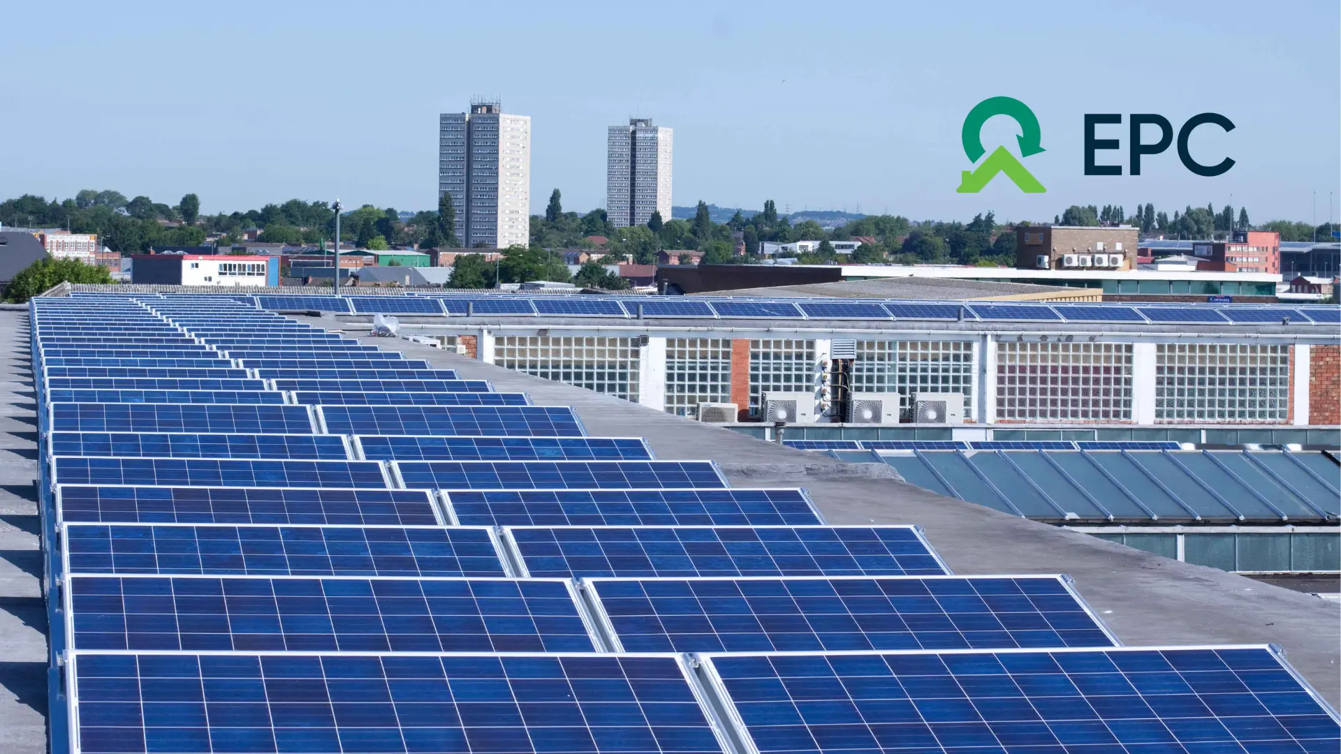 Rooftop solar panels on an industrial building with a cityscape and two tall buildings in the background. EPC logo in the top right corner.