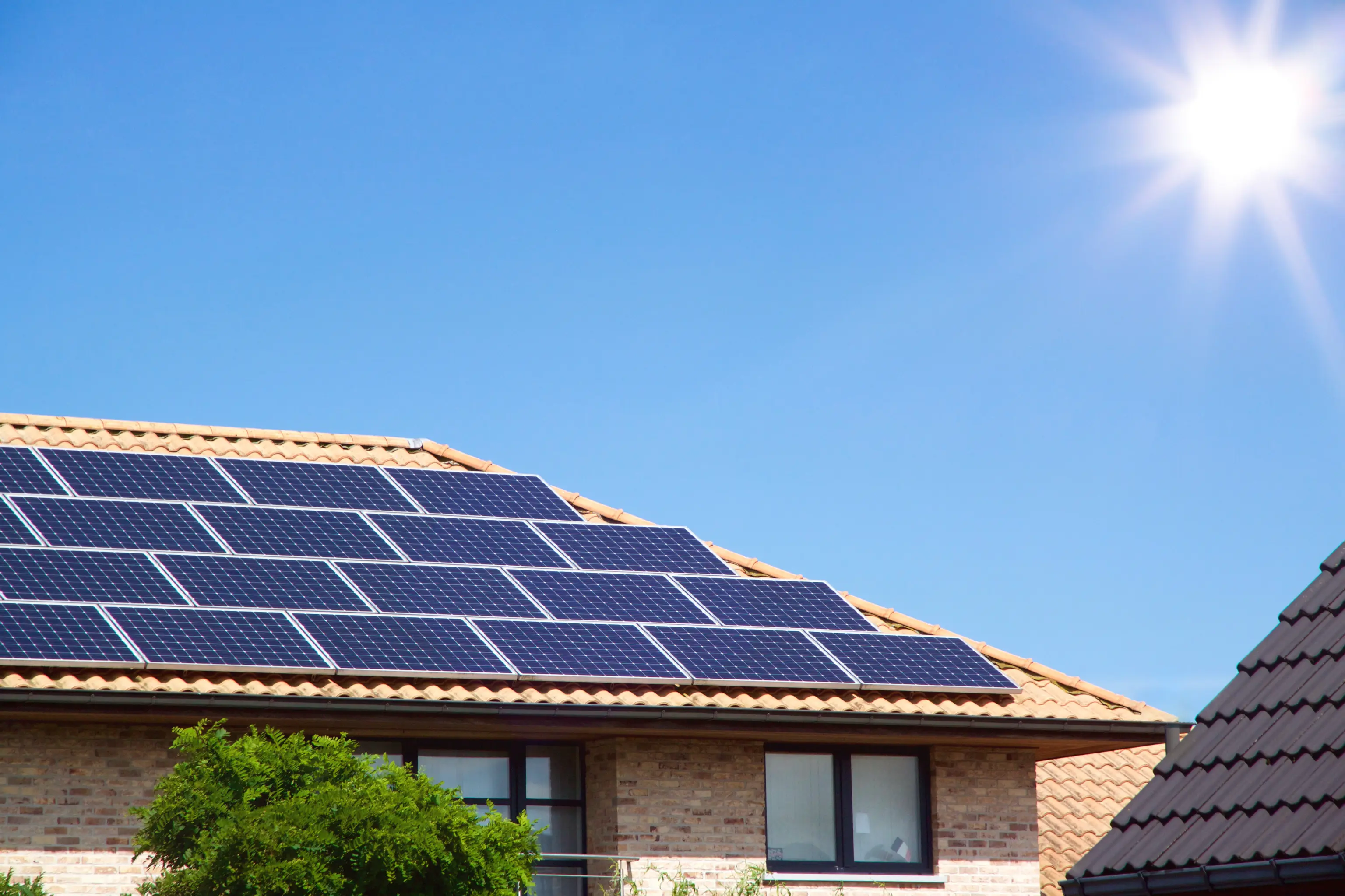 Solar panels on a house roof under a clear blue sky with the sun shining brightly.