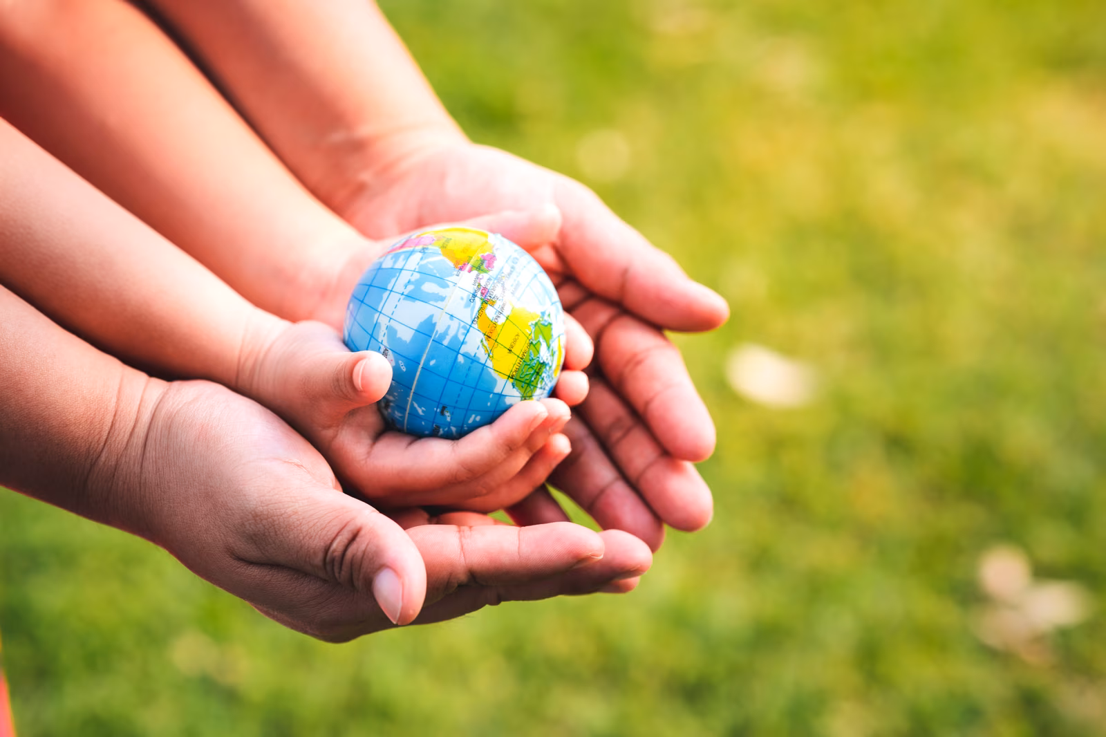 Adult and child hands holding a miniature globe outdoors